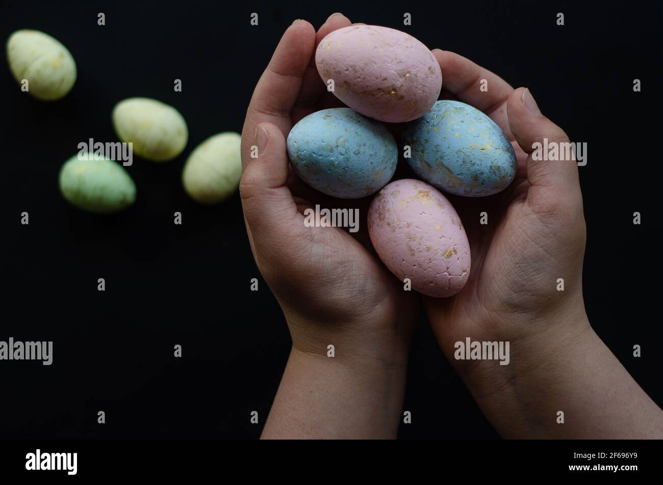 Oeufs de Pâques dans les mains et sur un fond sombre, place libre Banque D'Images