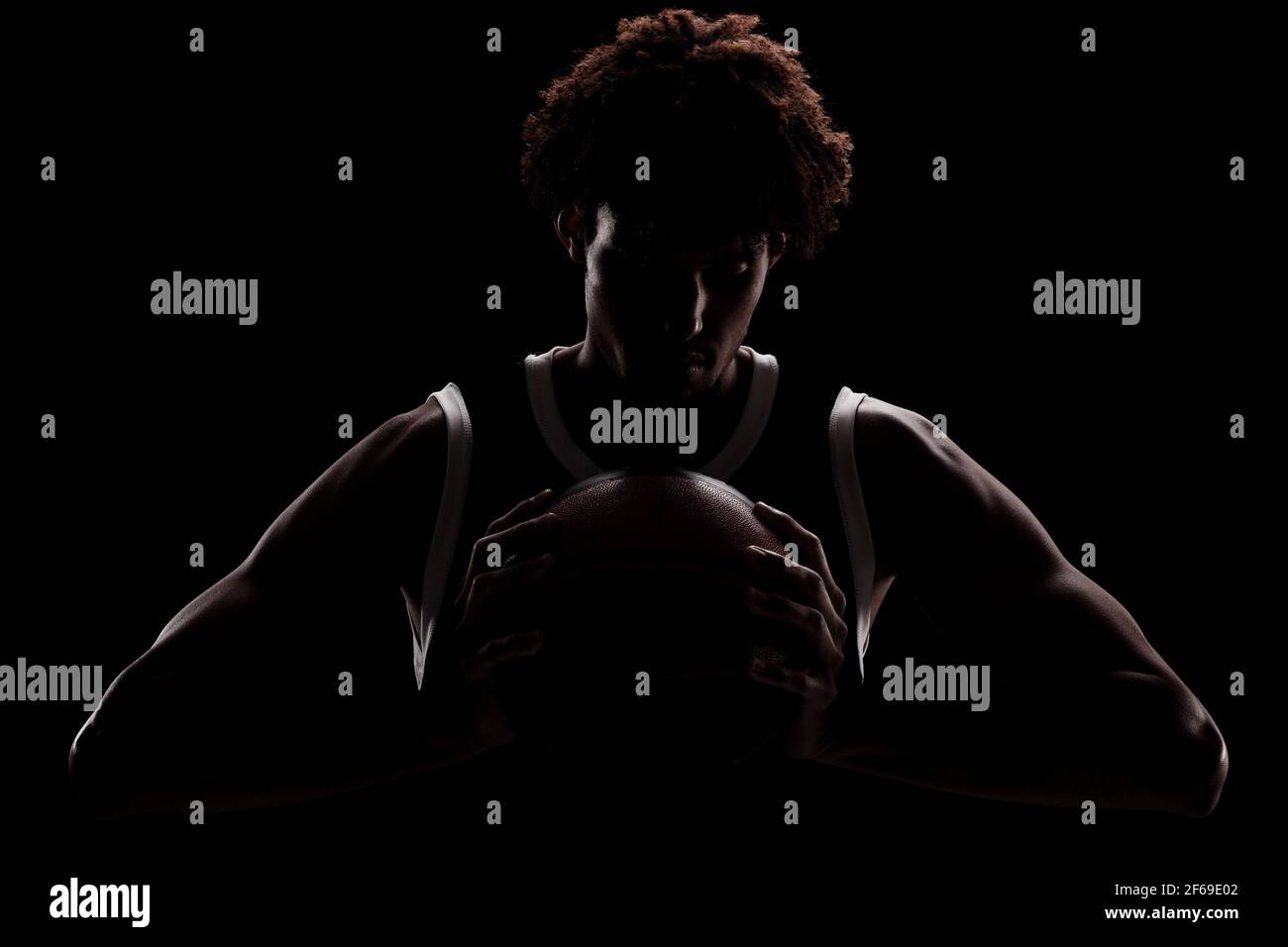 Joueur de basket-ball professionnel tenant une balle sur fond noir. Sérieux homme afro-américain concentré en uniforme sportif. Banque D'Images