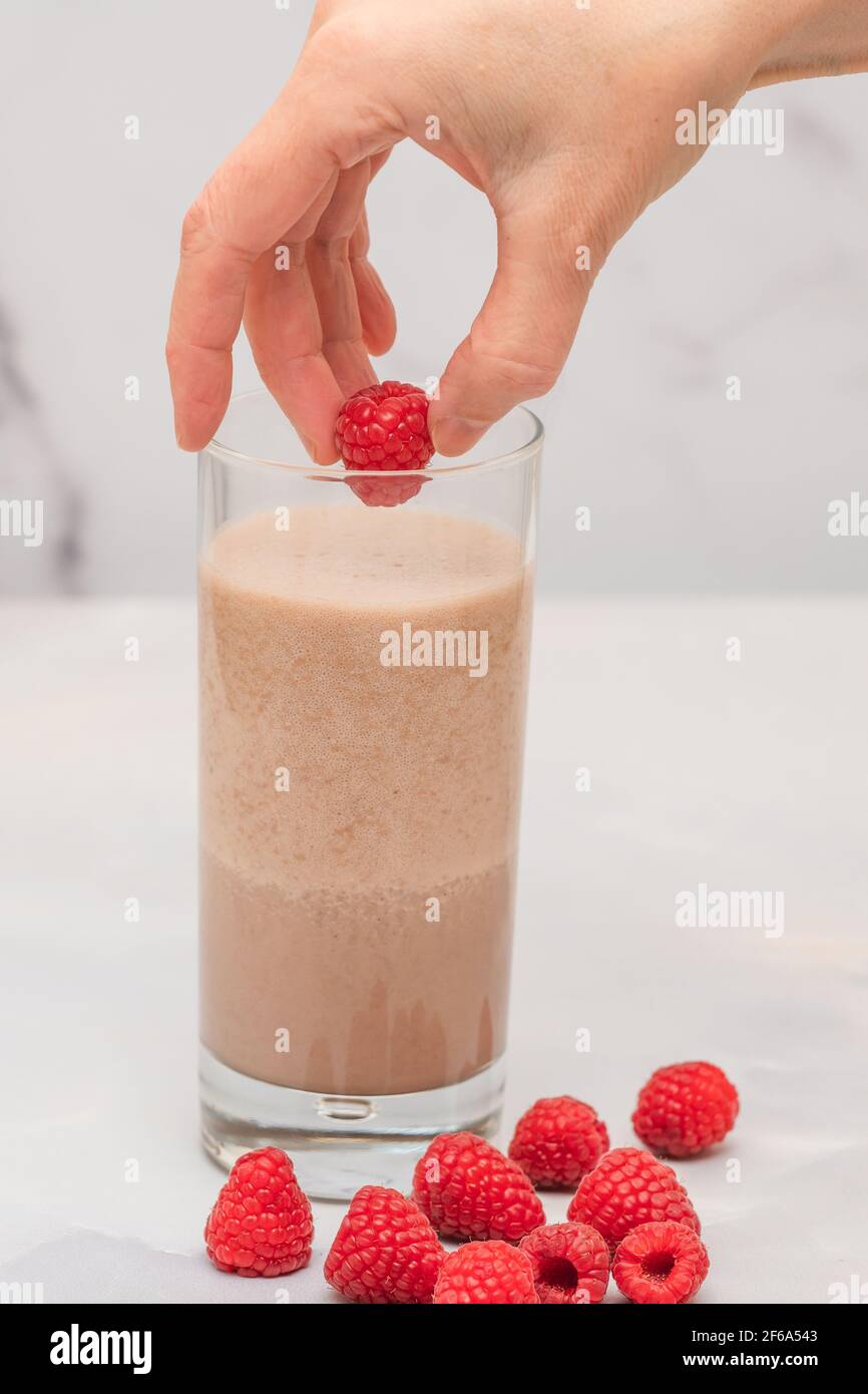 Milk shake au chocolat avec framboises fraîches gros plan sur fond de marbre, mains de femme, bannière verticale Banque D'Images