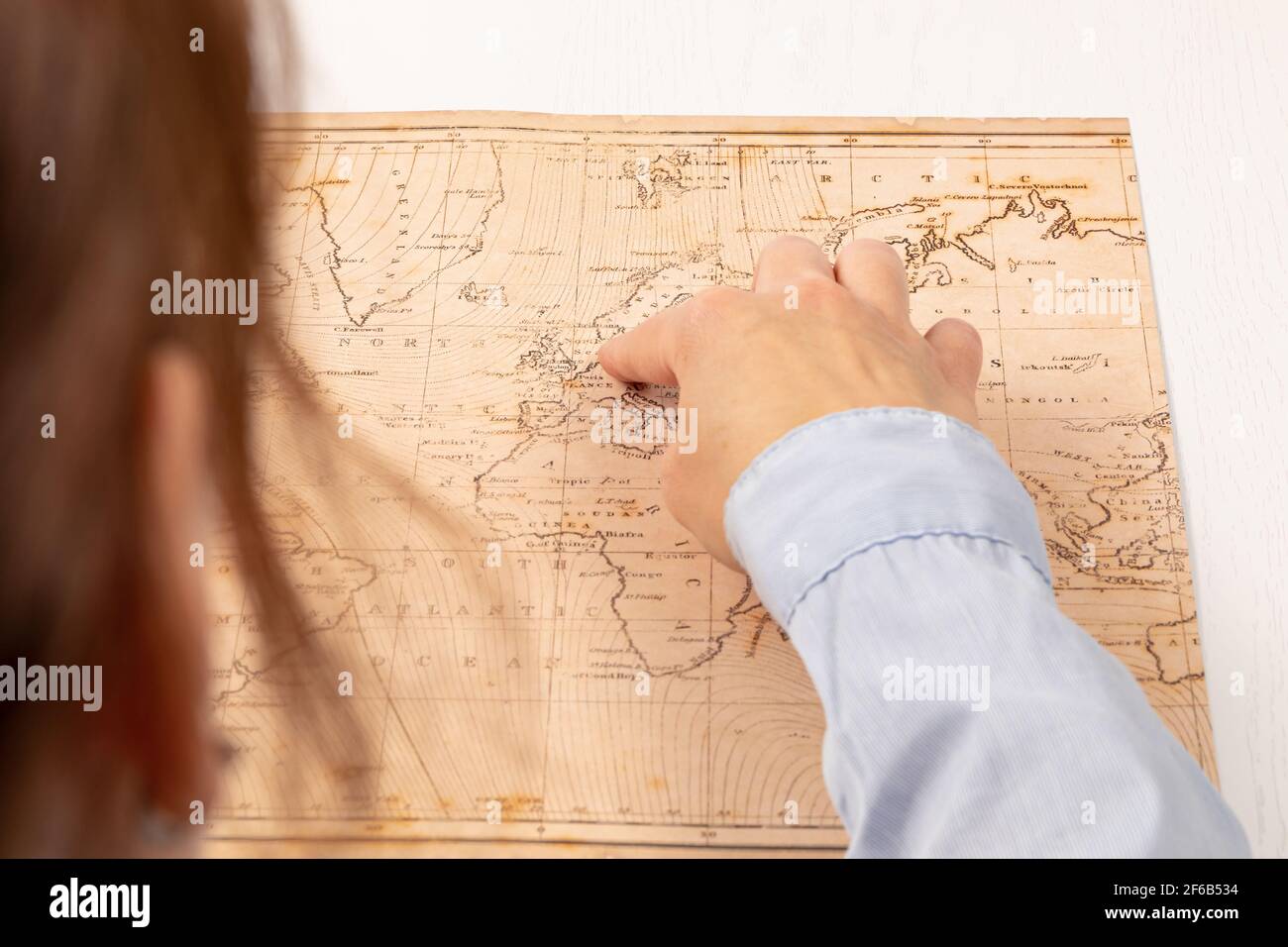 main femelle montre le lieu de voyage sur la carte du monde sur le fond d'une table en bois blanc. gros plan. mise au point sélective Banque D'Images