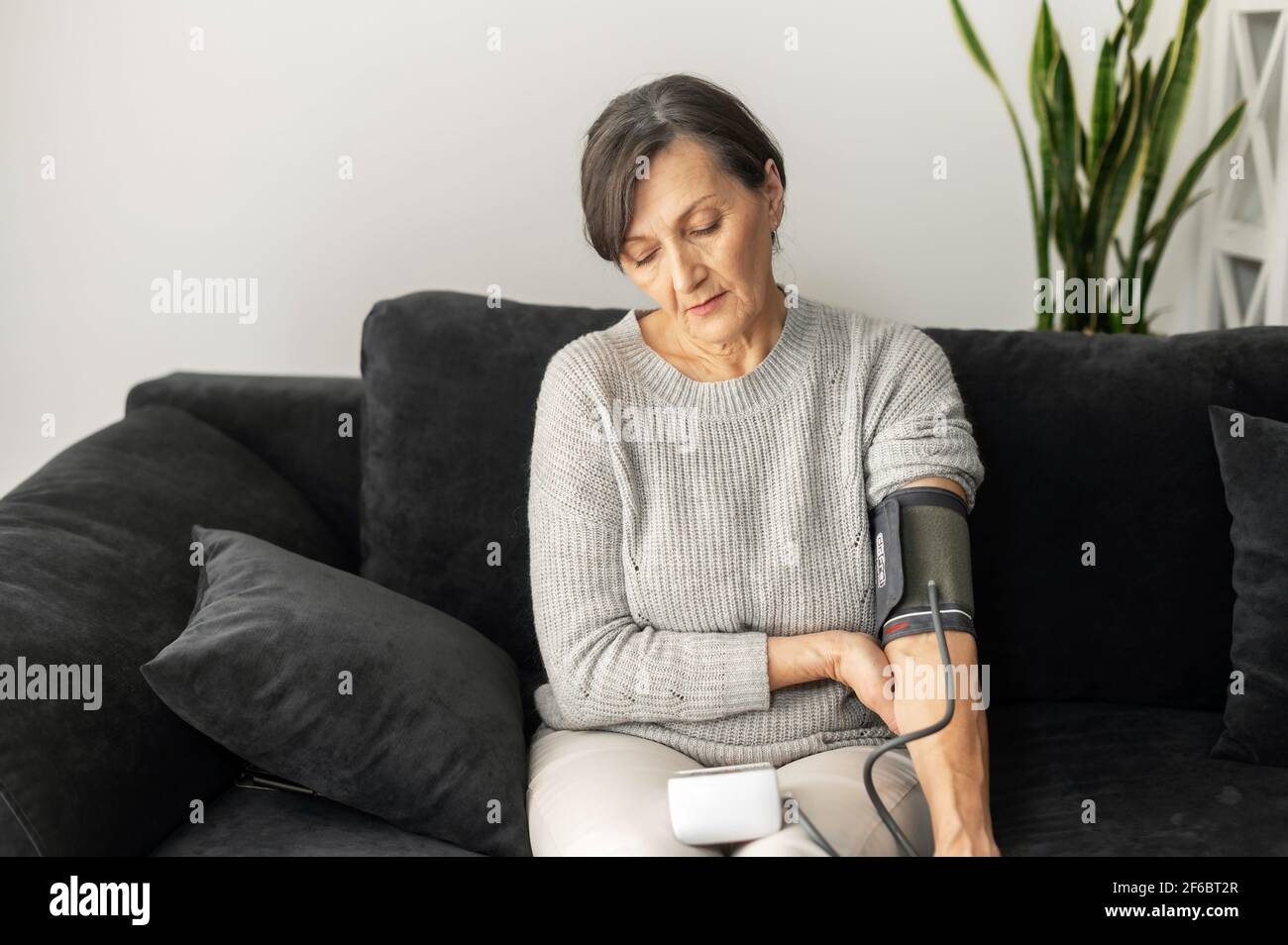 La femme âgée utilise le tonometr pour la santé auto-vérification assis sur le canapé, une femme âgée mesurant la tension artérielle à la maison. Concept de santé et de médecine Banque D'Images