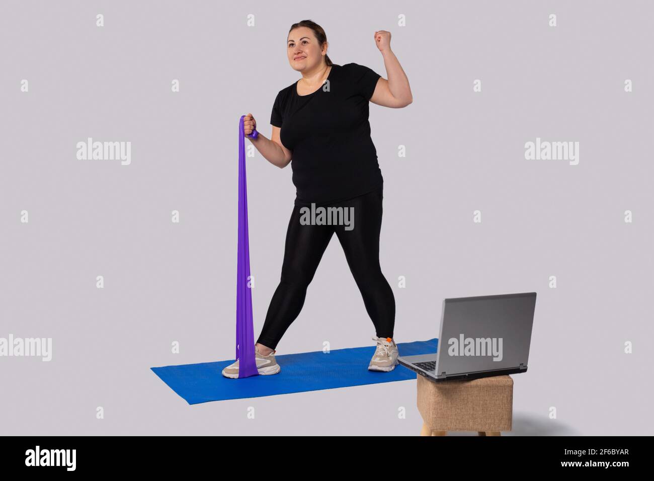 Fitness avec élastique.FAT Woman en vêtements de sport faisant de l'exercice avec un élastique sur le tapis de yoga en face de l'ordinateur portable.Un mode de vie sain.Sport et Banque D'Images