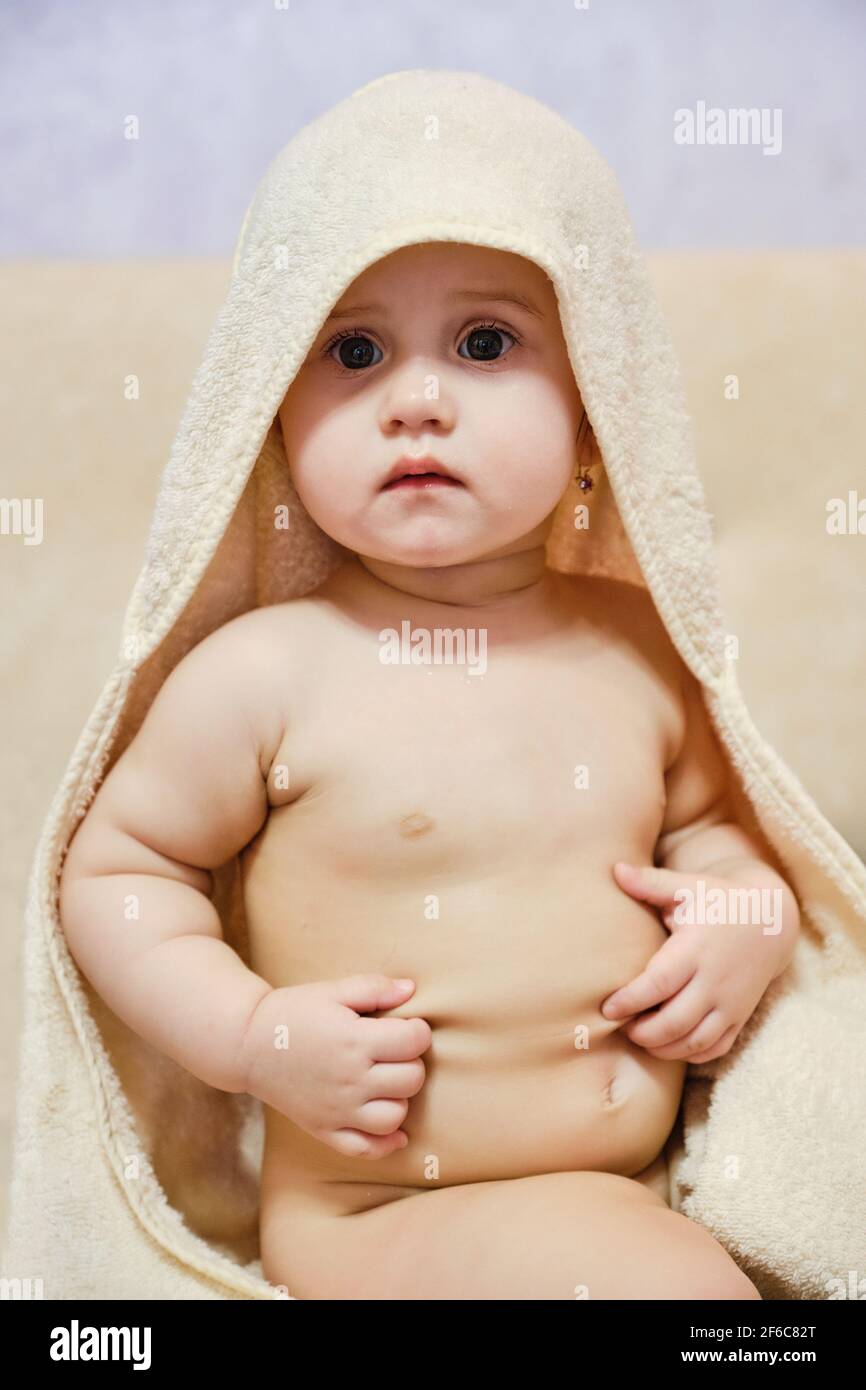Bébé fille après la douche ou le bain avec une serviette sur la tête. Bébé  portant une serviette à capuchon, assis sur le lit des parents après le  bain ou la douche.