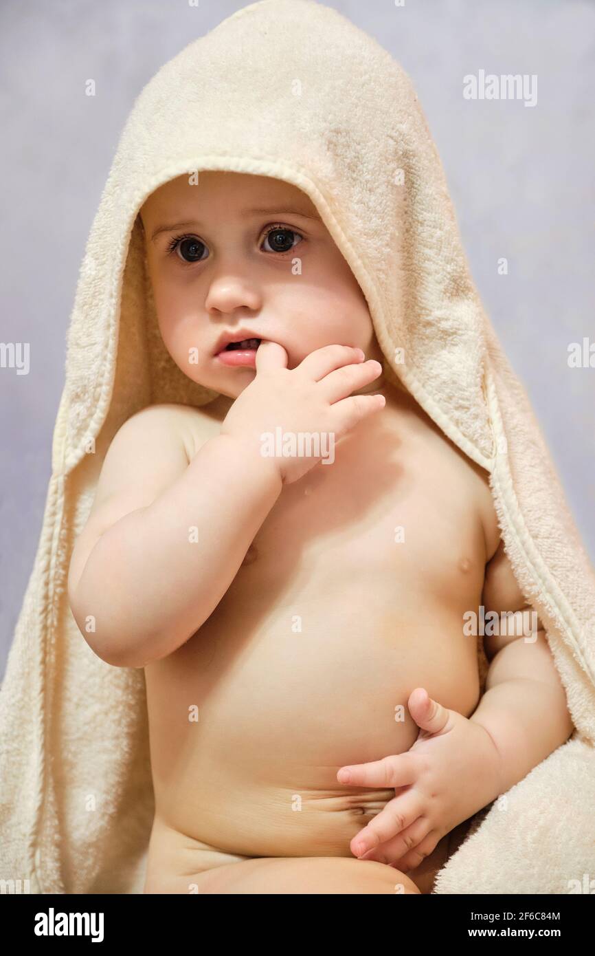 Bébé fille après la douche ou le bain avec une serviette sur la tête. Bébé  portant une serviette à capuchon, assis sur le lit des parents après le bain  ou la douche.