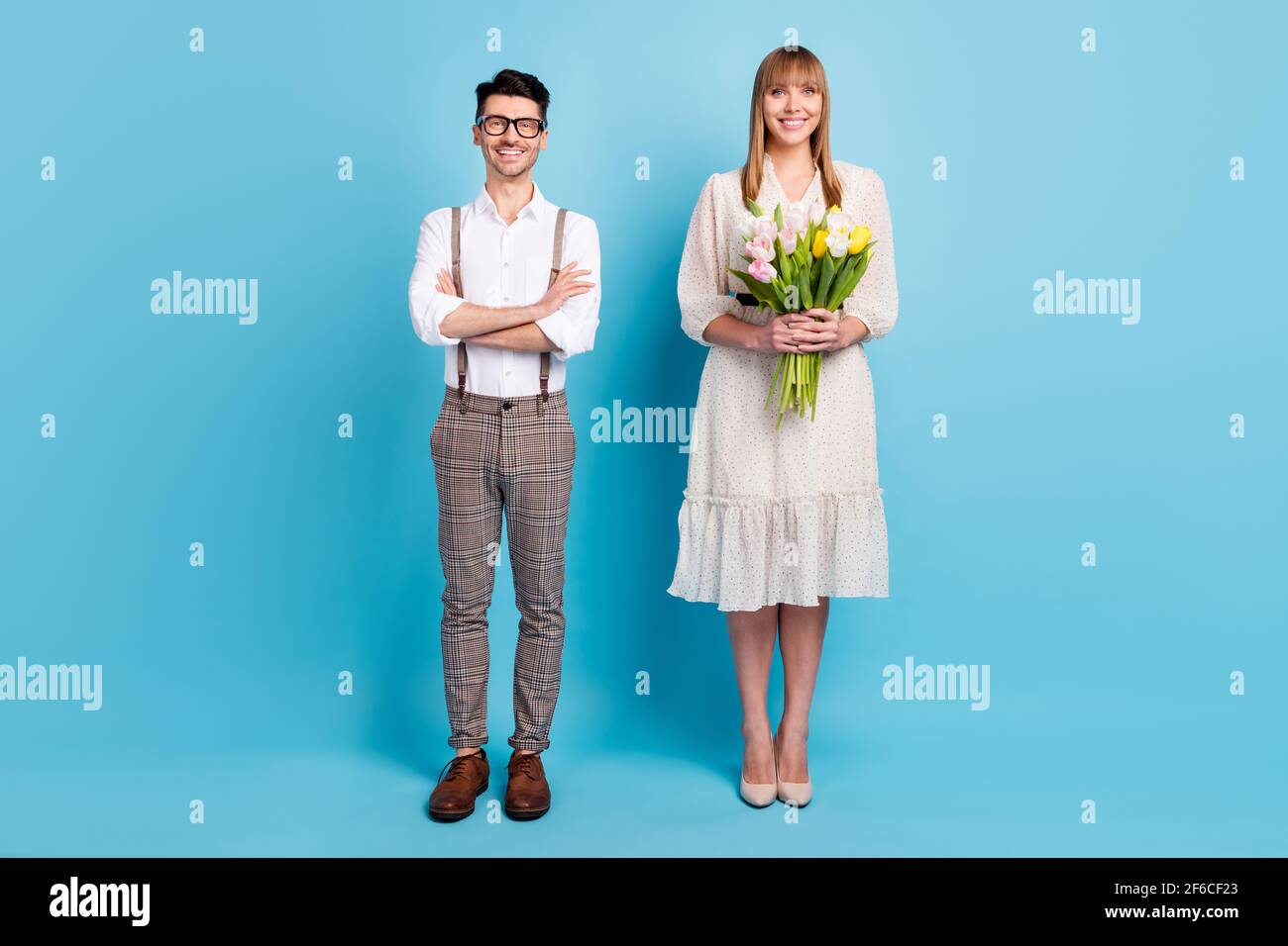 Photo de deux personnes adorables vêtues de vêtements blancs présentant bouquet de fleurs bras plié isolé couleur bleu fond Banque D'Images