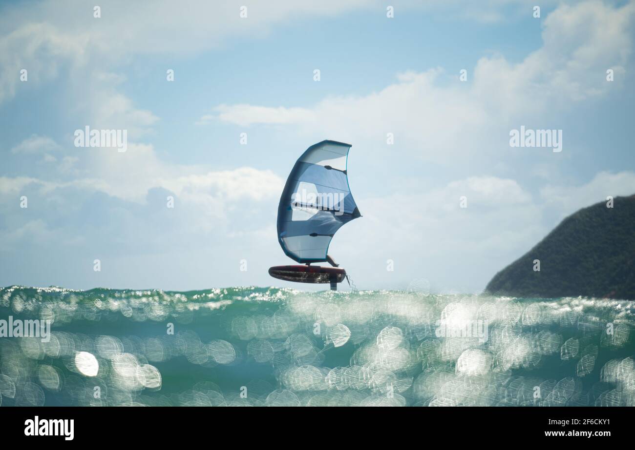 Une aile d'homme fait des feuilles en mer à l'aide d'une aile gonflable à la main, à cheval sur une planche de surf hydrofoil. Mer turquoise, ciel bleu ciel nuageux. Banque D'Images