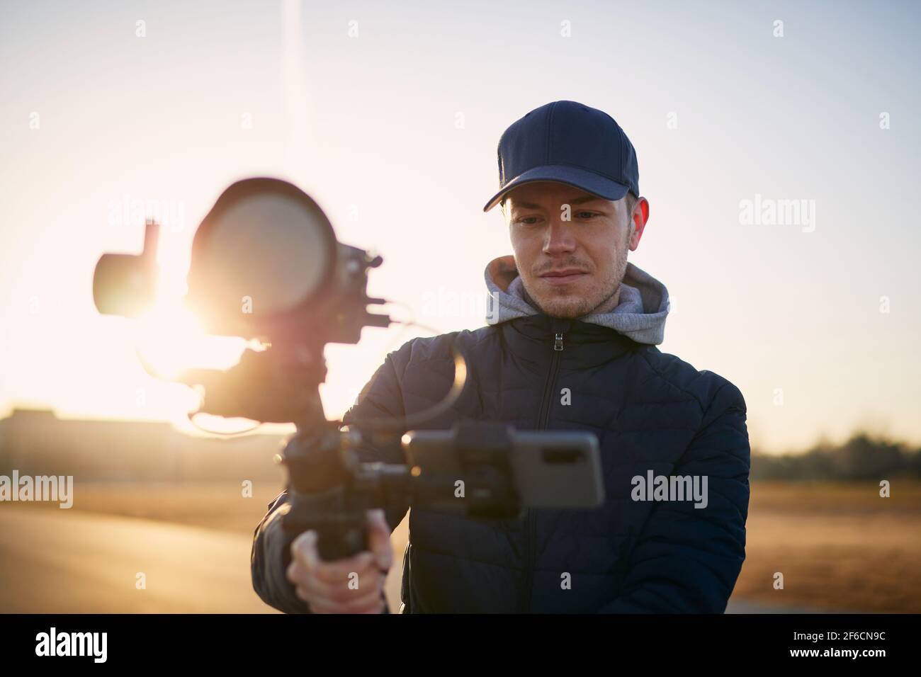 Jeune homme filmant avec caméra et nacelle. Portrait du vidéaste au beau lever du soleil. Banque D'Images