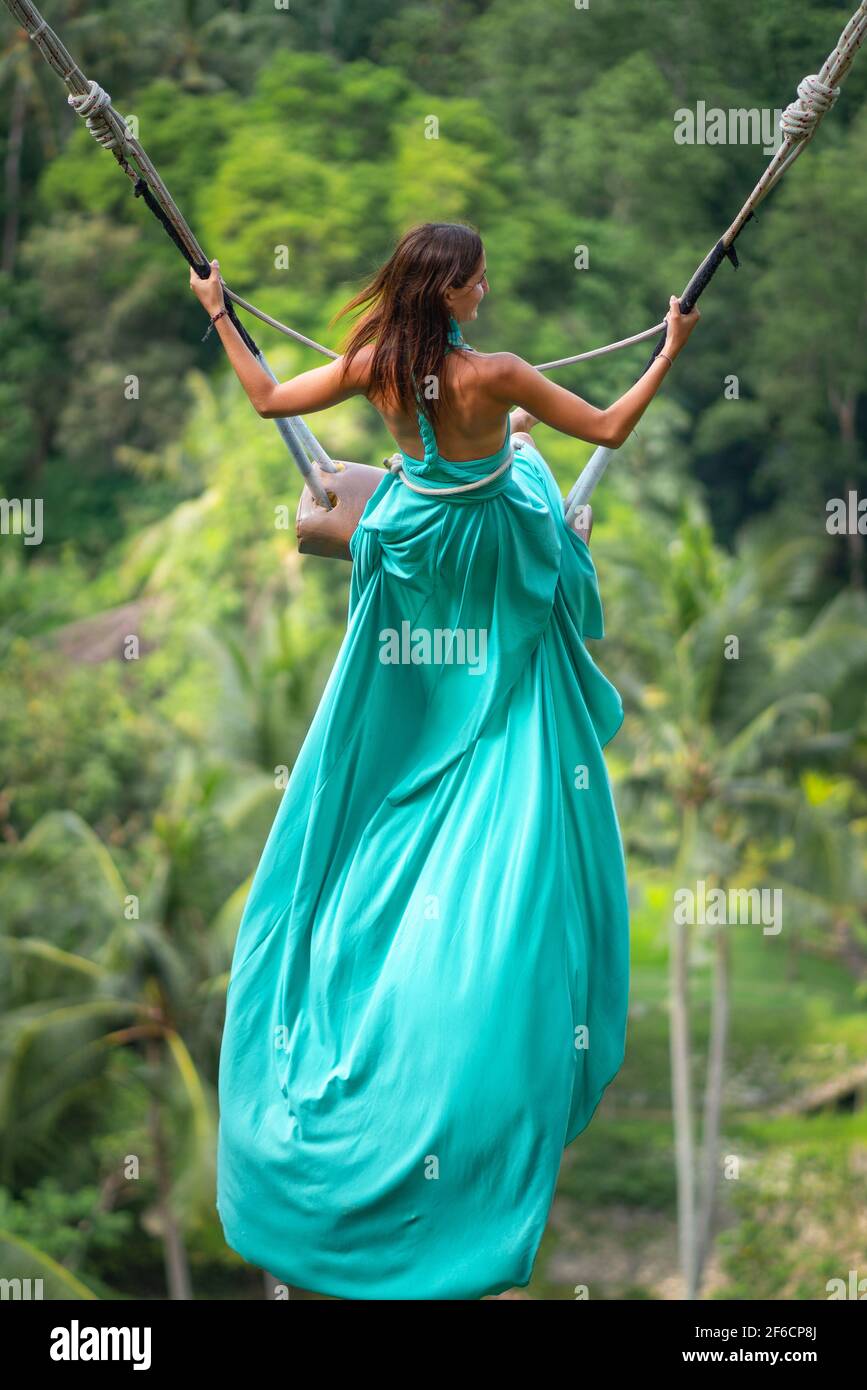 Une jeune femme bronzee qui fait une longue balancoire en robe turquoise. Ile de Bali. Foret tropicale en arriere plan. Voyage et joie. Gros plan Photo Stock Alamy