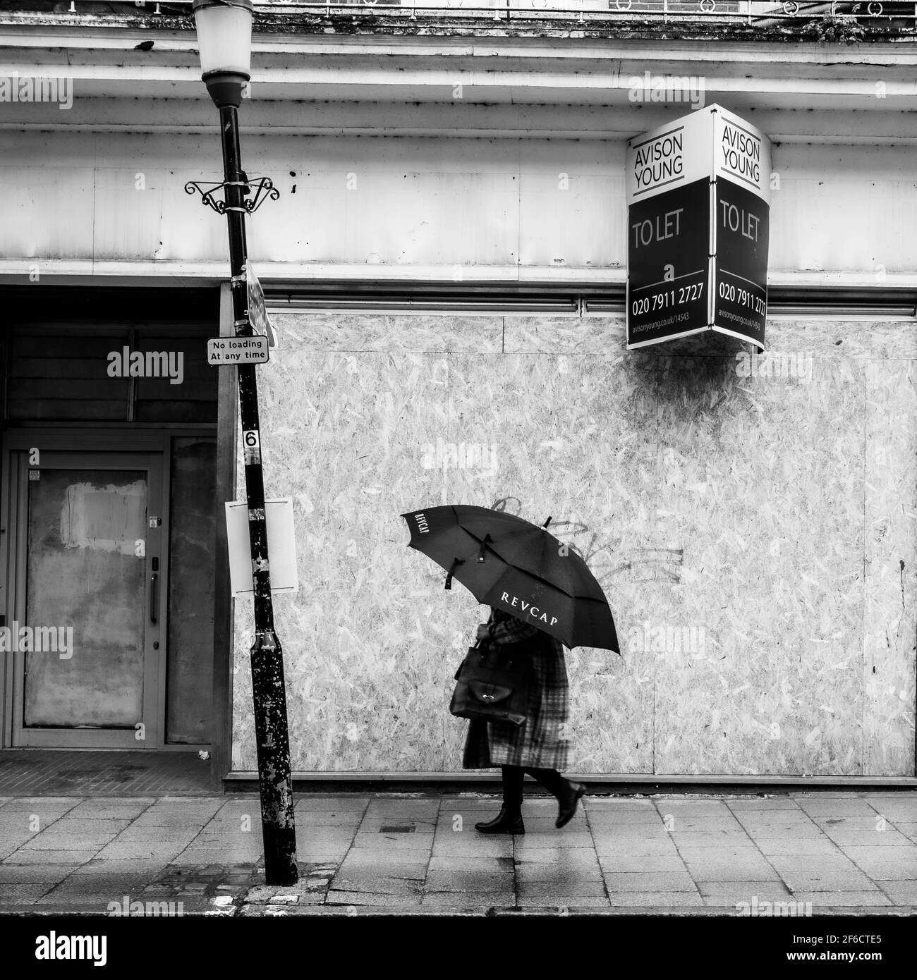 Noir et blanc image d'UNE femme sous un parapluie Passer devant UN magasin de détail fermé de High Street Banque D'Images
