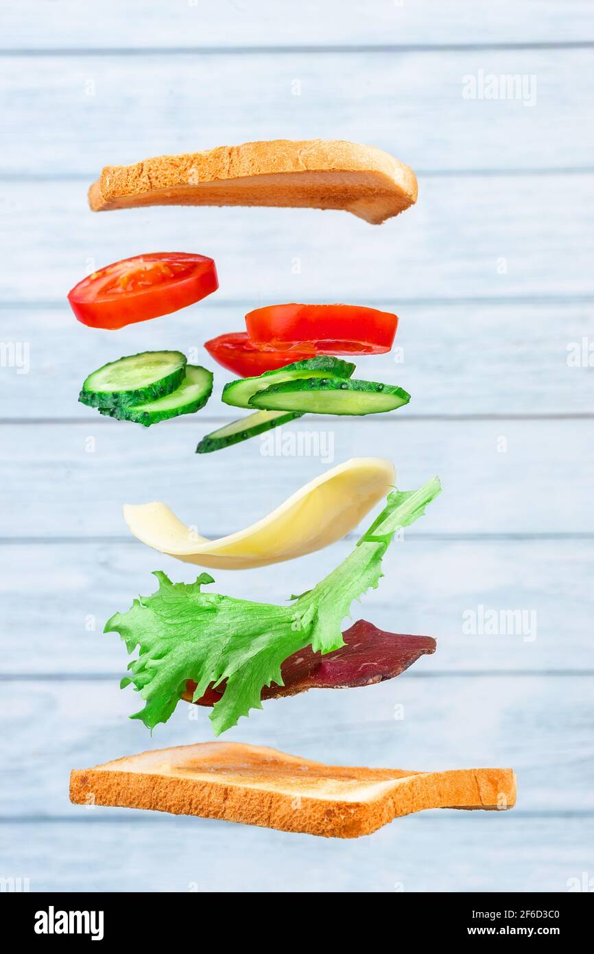 Des couches volantes de sandwich avec du jambon, du fromage et des légumes sur fond de bois. Concept de la nourriture pour le petit déjeuner Banque D'Images