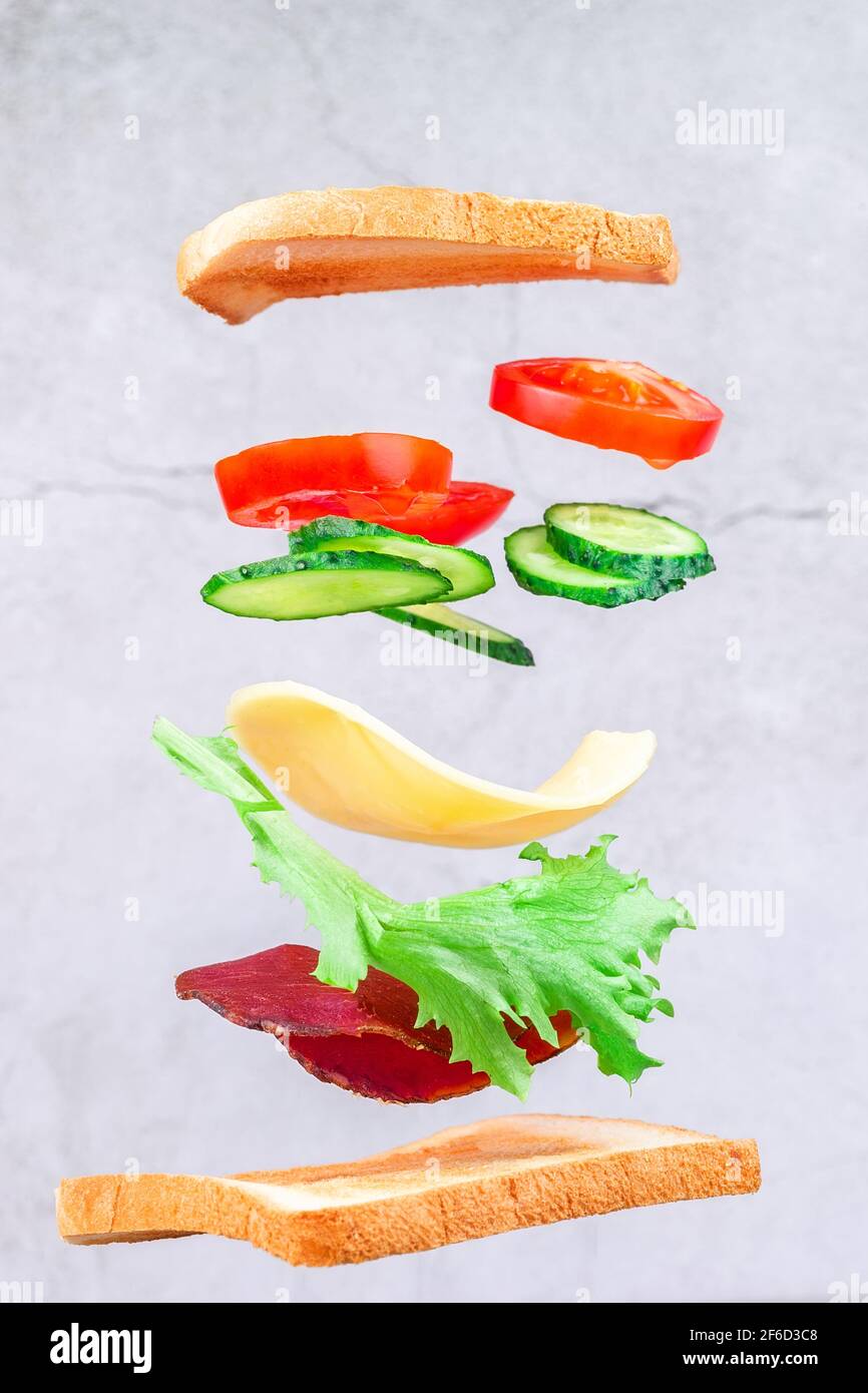 Des couches volantes de sandwich avec du jambon, du fromage et des légumes sur fond de bois. Concept de la nourriture pour le petit déjeuner Banque D'Images