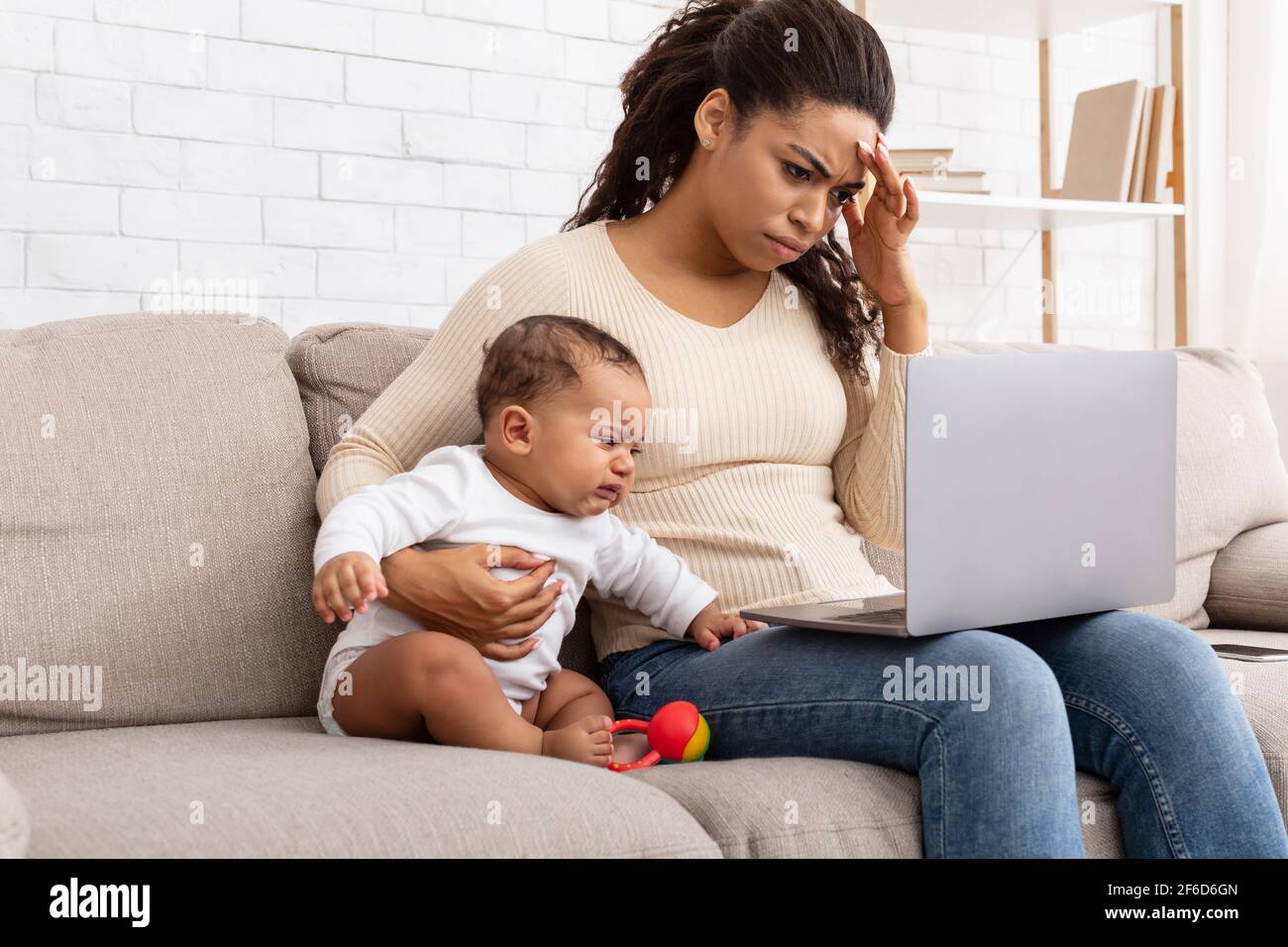 Mère africaine fatiguée avec bébé plant utilisant un ordinateur portable à la maison Banque D'Images