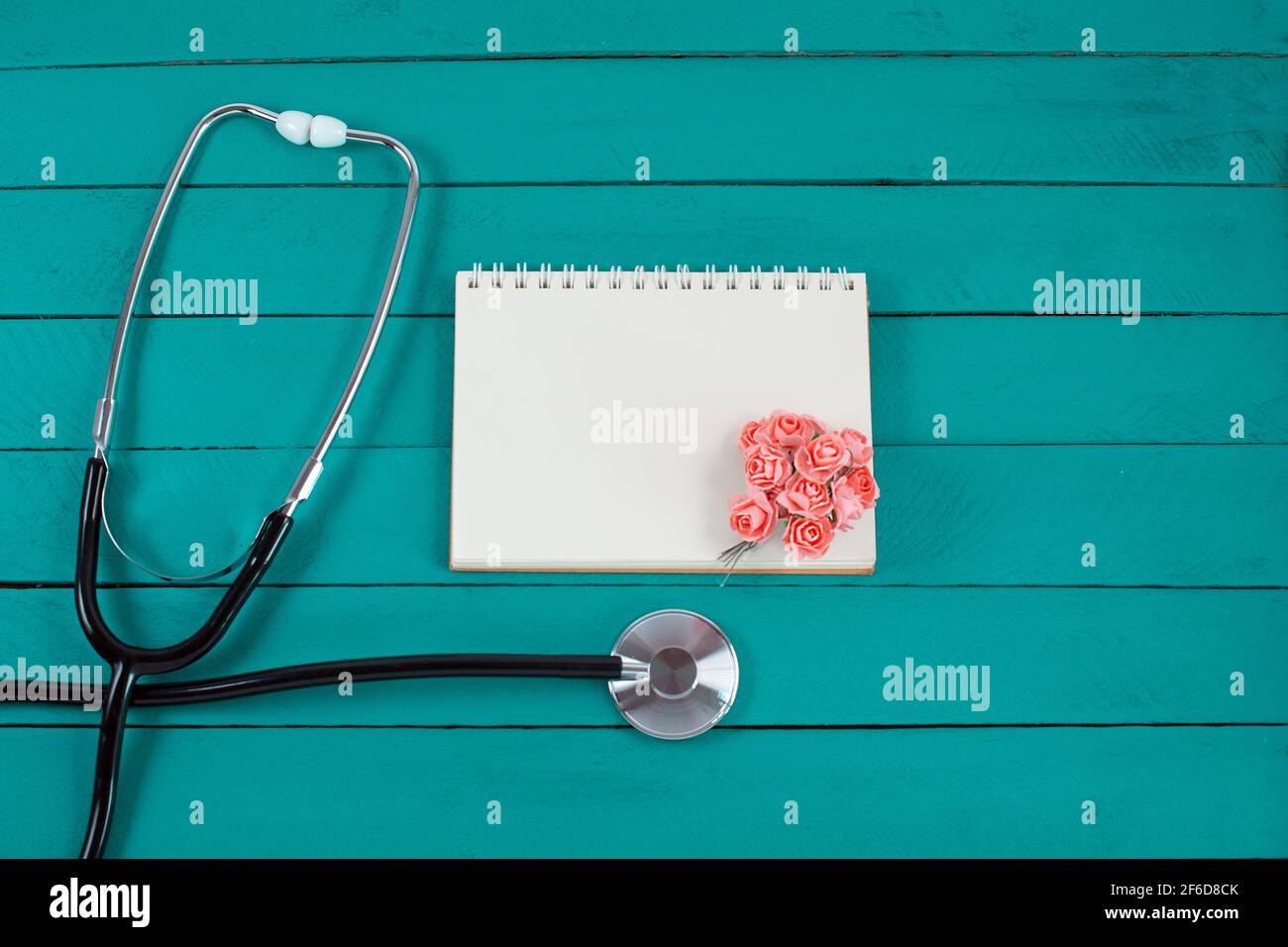 Stéthoscope avec petites fleurs et carnet sur fond bleu en bois. Copier l'espace. Banque D'Images