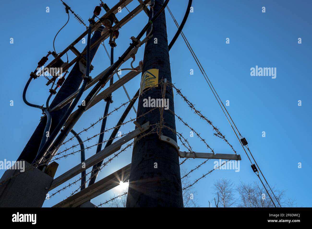 Alimentation électrique en hauteur 33KV montée sur des poteaux en bois et protégée par une barrière à fil bardé. Banque D'Images