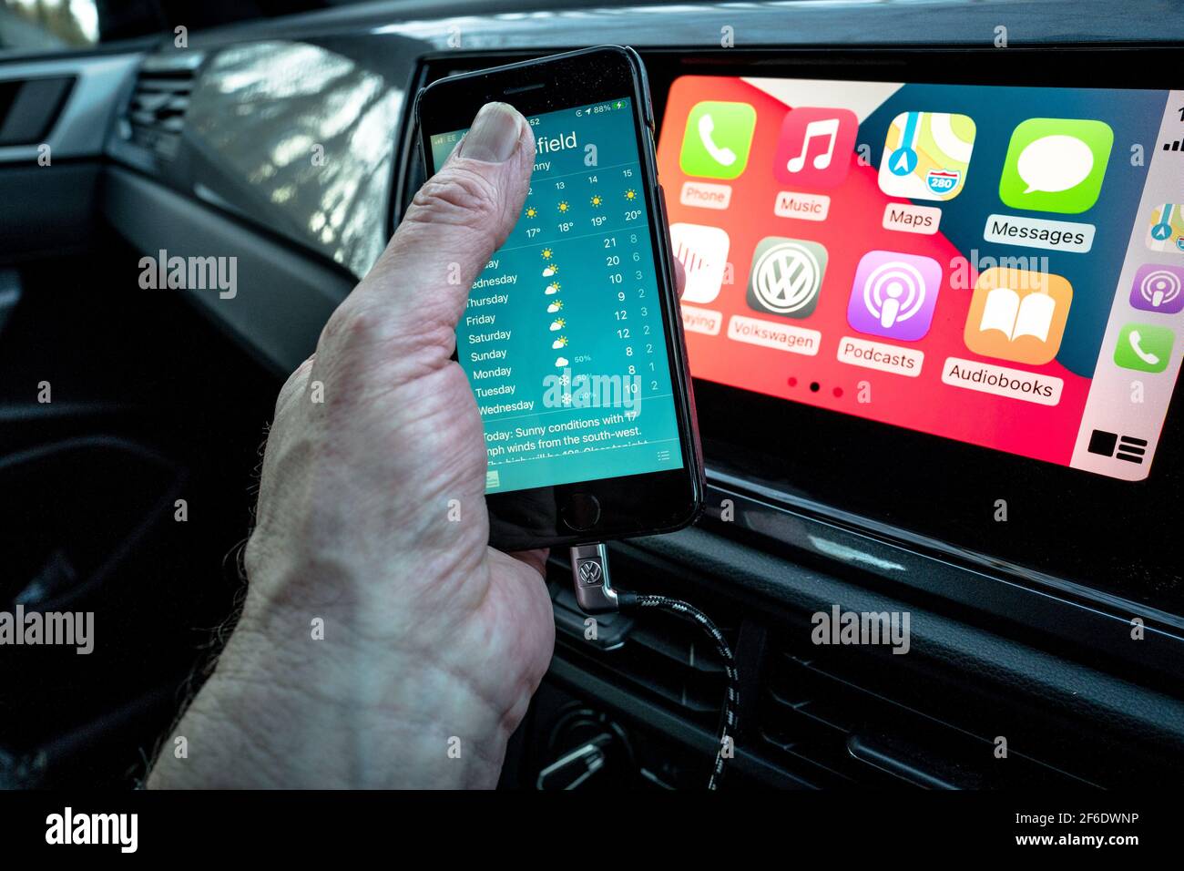 Un homme utilisant son Apple iphone se connecte aussi à l'unité de divertissement et de communication dans un VW Polo. Banque D'Images