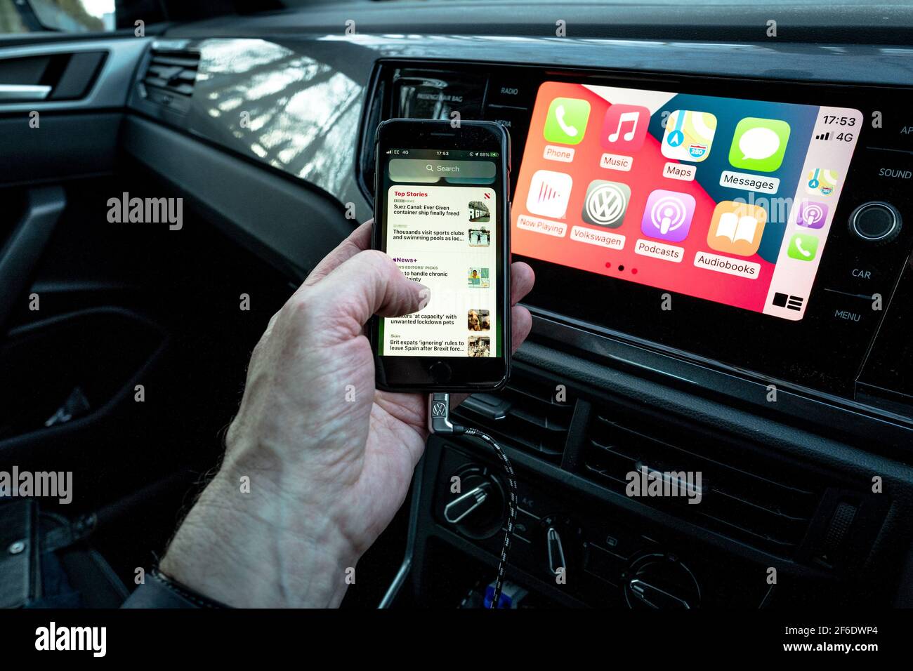 Un homme utilisant son Apple iphone se connecte aussi à l'unité de divertissement et de communication dans un VW Polo. Banque D'Images