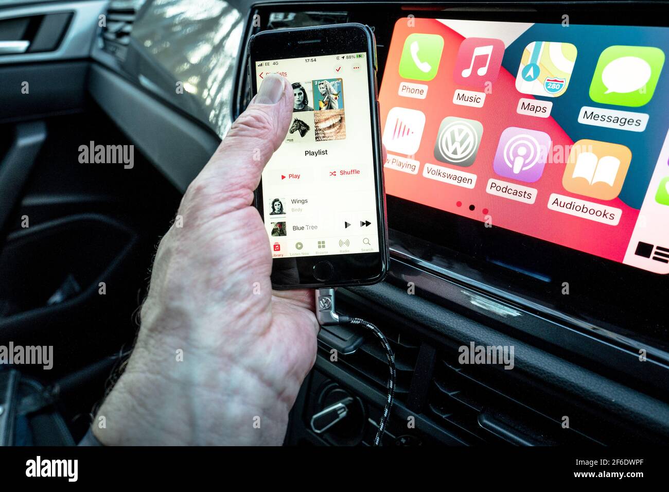 Un homme utilisant son Apple iphone se connecte aussi à l'unité de divertissement et de communication dans un VW Polo. Banque D'Images