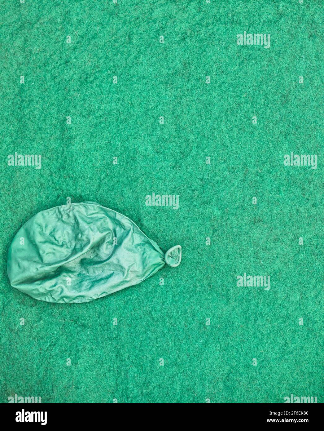 Ballon vert dégonflé isolé sur fond vert texturé. Concept de triste, malheureux, épuisé, destruction Banque D'Images