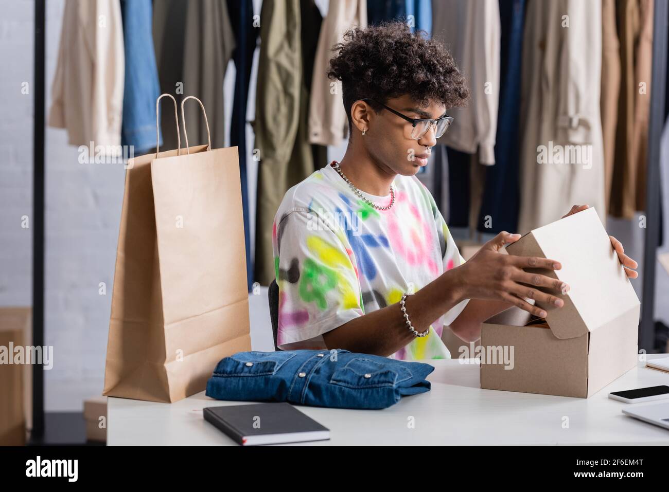 Propriétaire de petite entreprise afro-américaine tenant une boîte près d'un sac de shopping et des vêtements dans la salle d'exposition Banque D'Images