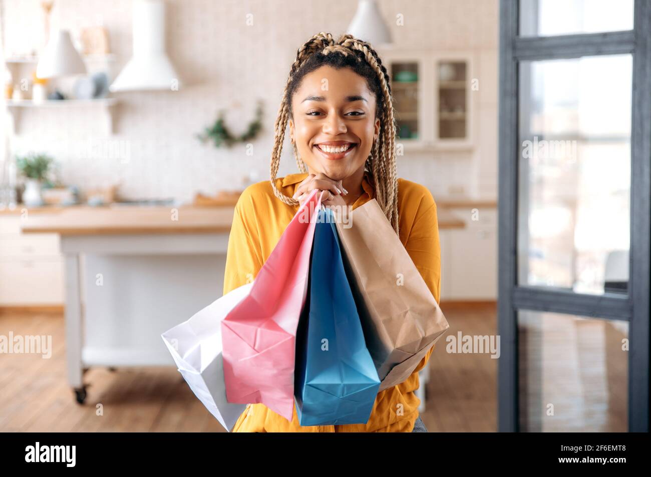 Une jeune femme afro-américaine heureuse avec des dreadlocks est assise dans le salon, se réjouit des choses achetées, presse des paquets de papier pour elle-même, regarde la caméra, sourit Banque D'Images