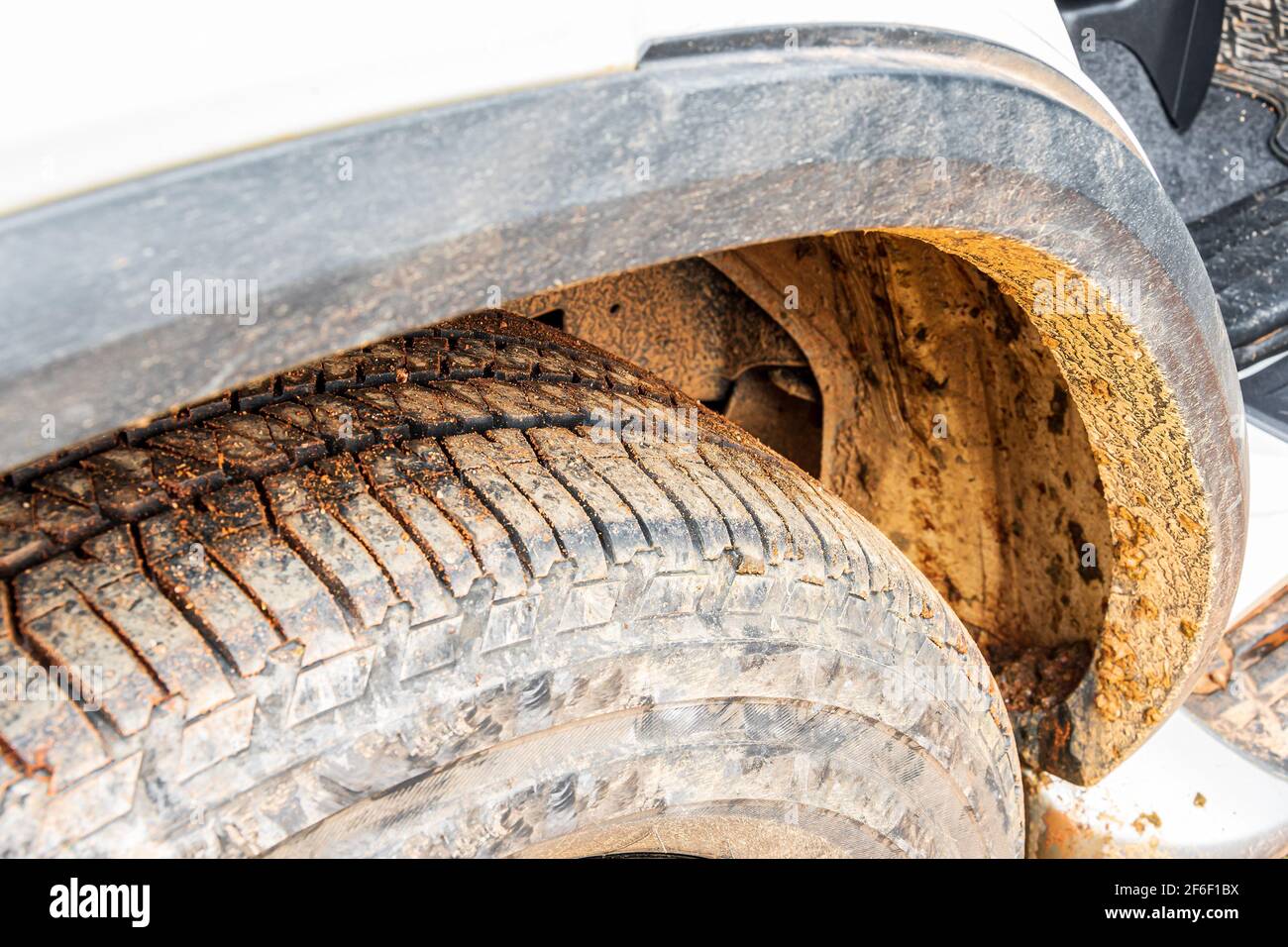Gros plan sur les pneus d'une voiture tout-terrain avec des pneus sales  d'une route sale. Saleté, poussière et petites pierres sur le pneu et boue  sur le pare-chocs. Aventure hors route en