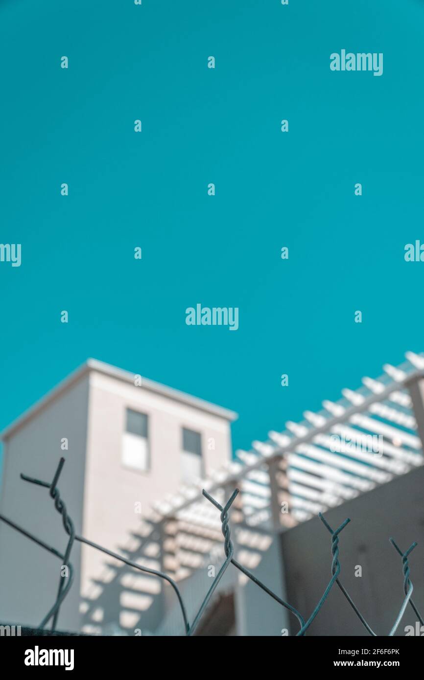 Bâtiment blanc au ciel turquoise clair avec clôture en premier plan. Couleurs pastel, minimalisme coloré créatif. Copier l'espace pour le texte. Banque D'Images