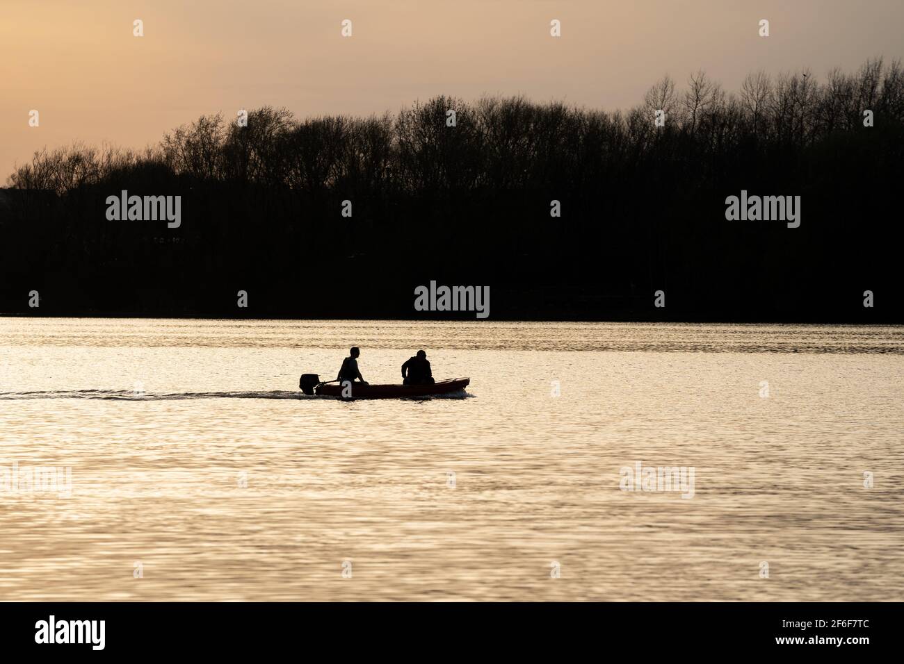 les gens dans la silhouette de bateau à grande vitesse au coucher du soleil sur le lac avec lumière dorée reflétant sur l'eau de la rivière voile rapidement pour sauver les nageurs. Réservoir eau calme Banque D'Images