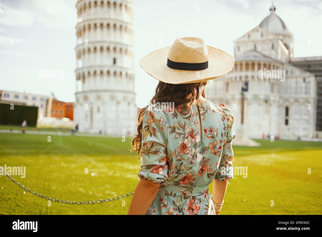 Vue de derrière une femme voyageur en robe fleurie avec chapeau visite près de la Tour de Pise, Italie. Banque D'Images