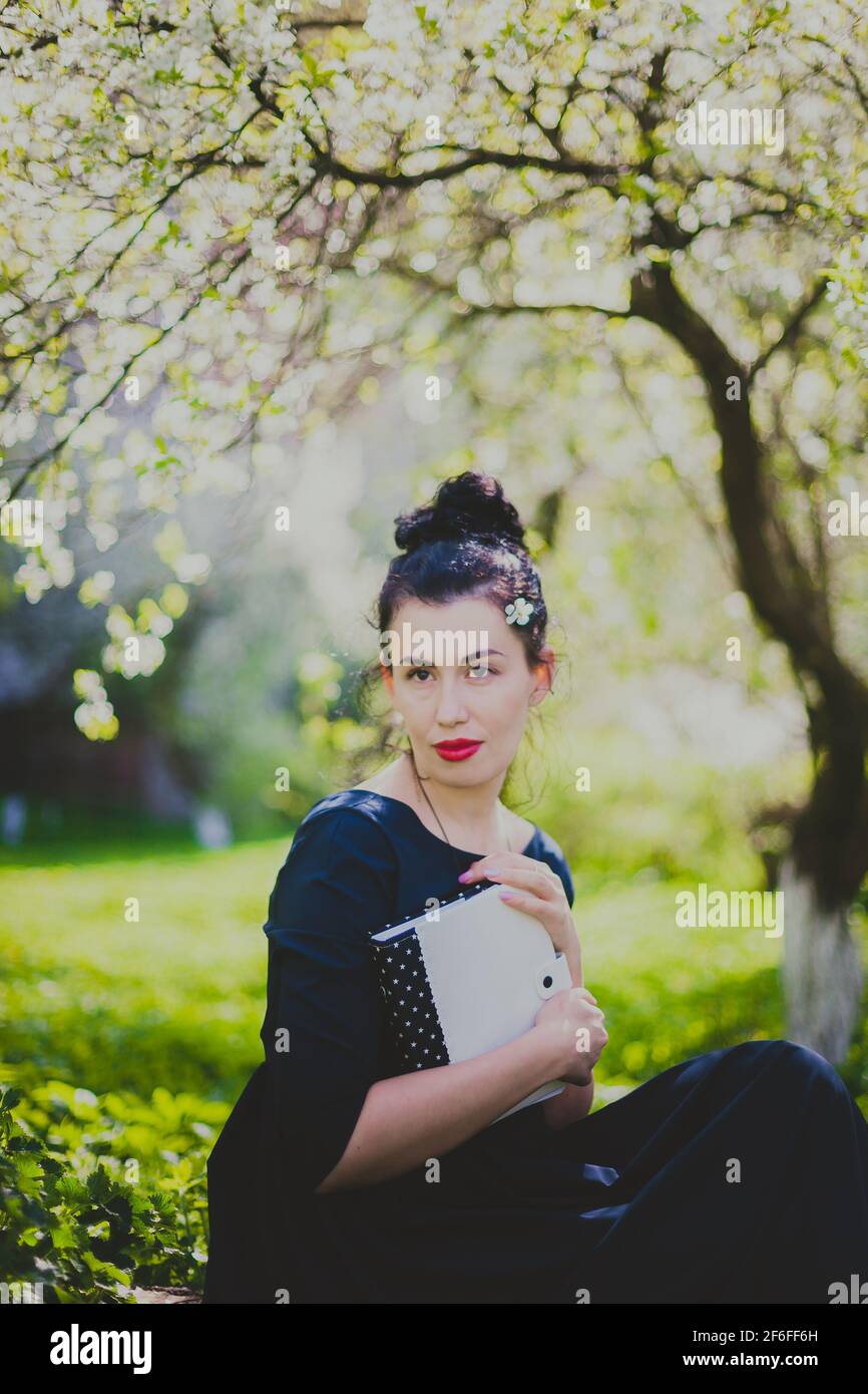 Femme heureuse assise dans le jardin de cerisier de printemps Banque D'Images