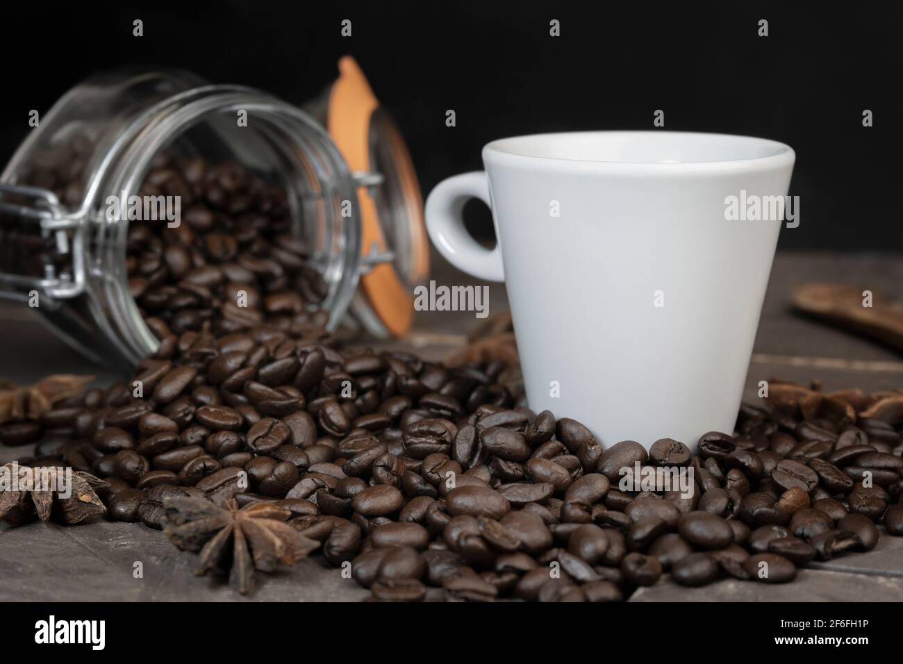 Grains de café dans un pot en verre avec une tasse de café blanc. Concept de boisson énergétique à base de caféine sur fond sombre. Banque D'Images