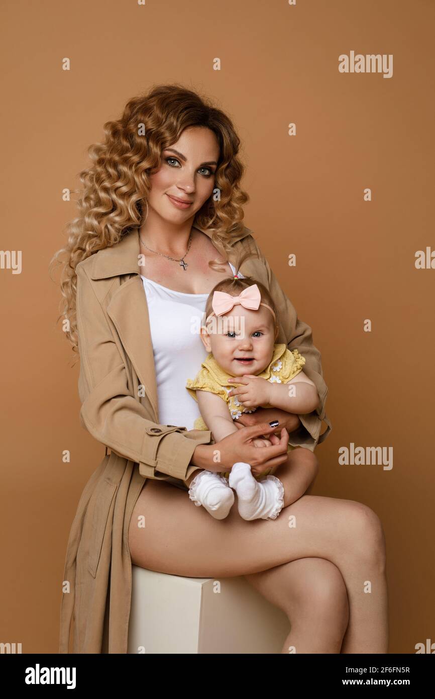 Magnifique Femme Dans Une Tranchee Beige Avec Une Petite Fille Et Un Haut Blanc Tenant Bebe Fille Mignon Dans Les Bras Assis Sur Blanc Contre Fond Peche Photo Stock Alamy