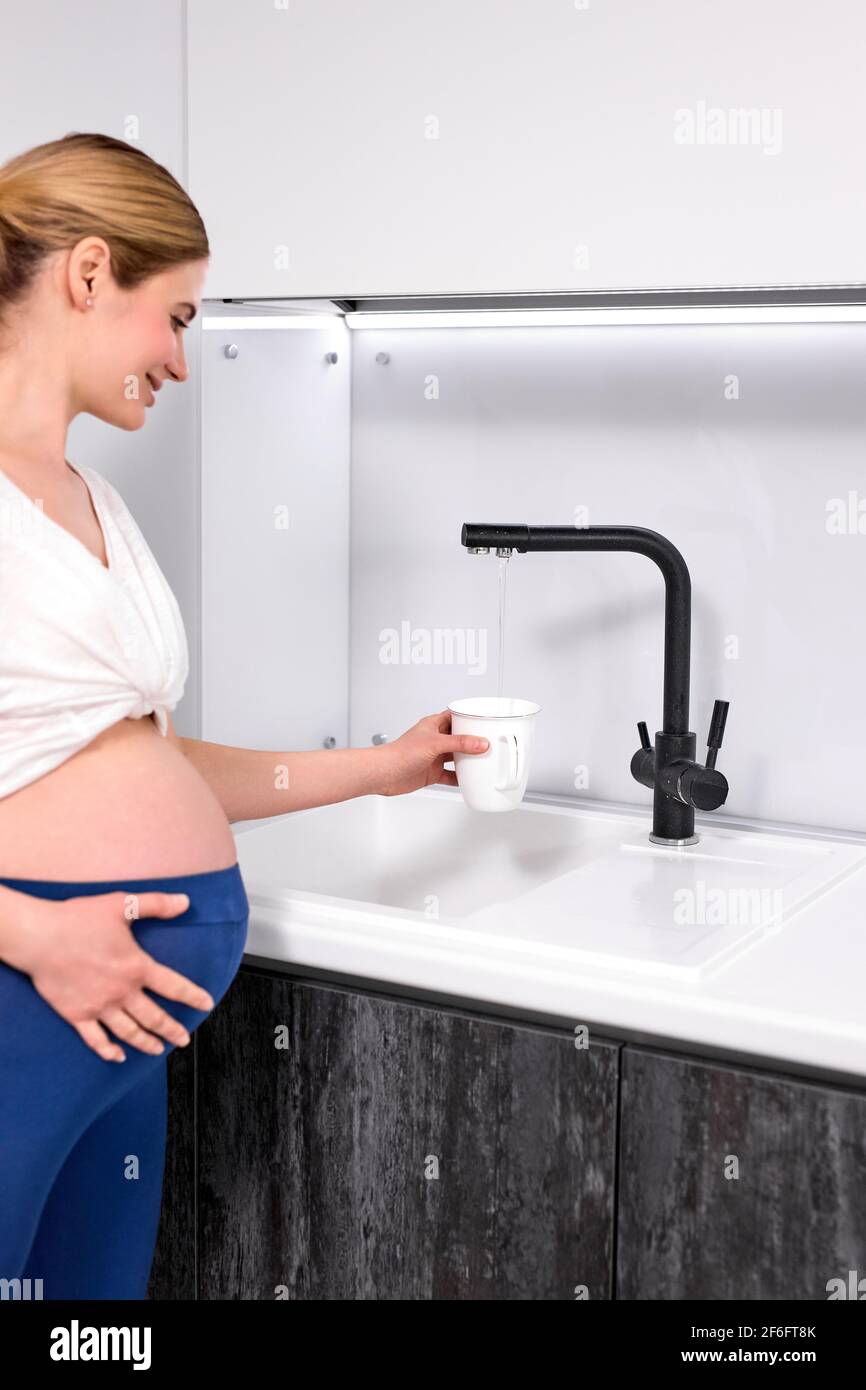 la femme enceinte se tient près du robinet remplit d'eau pour boire après  l'entraînement, vue latérale sur la femme avec grand ventre, à la maison  Photo Stock - Alamy