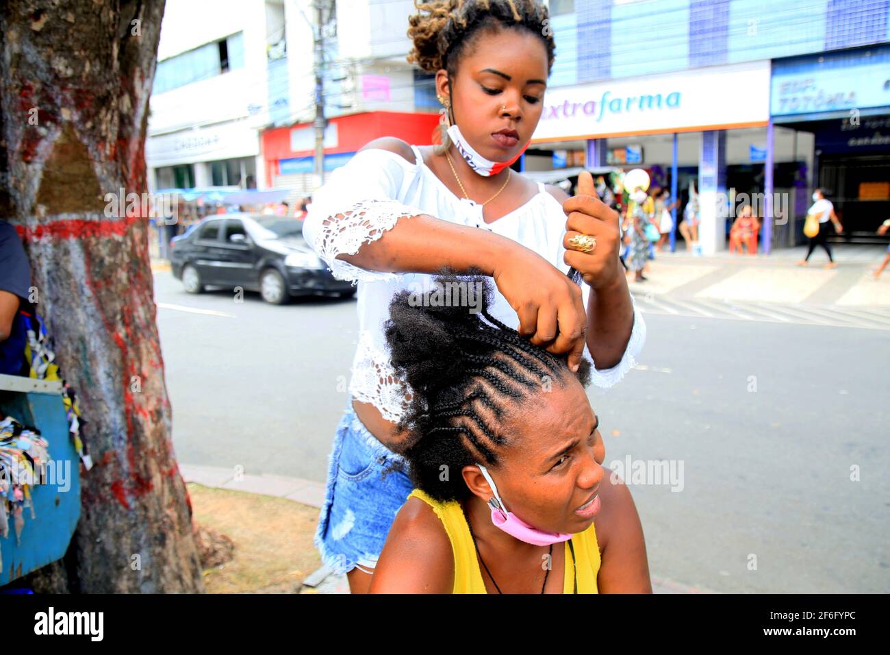 salvador, bahia, brésil - 14 décembre 2020 : On voit un jeune homme faire des papillons afro sur les cheveux d'une femme noire dans la rue du centre-ville de Salvador. *** Banque D'Images