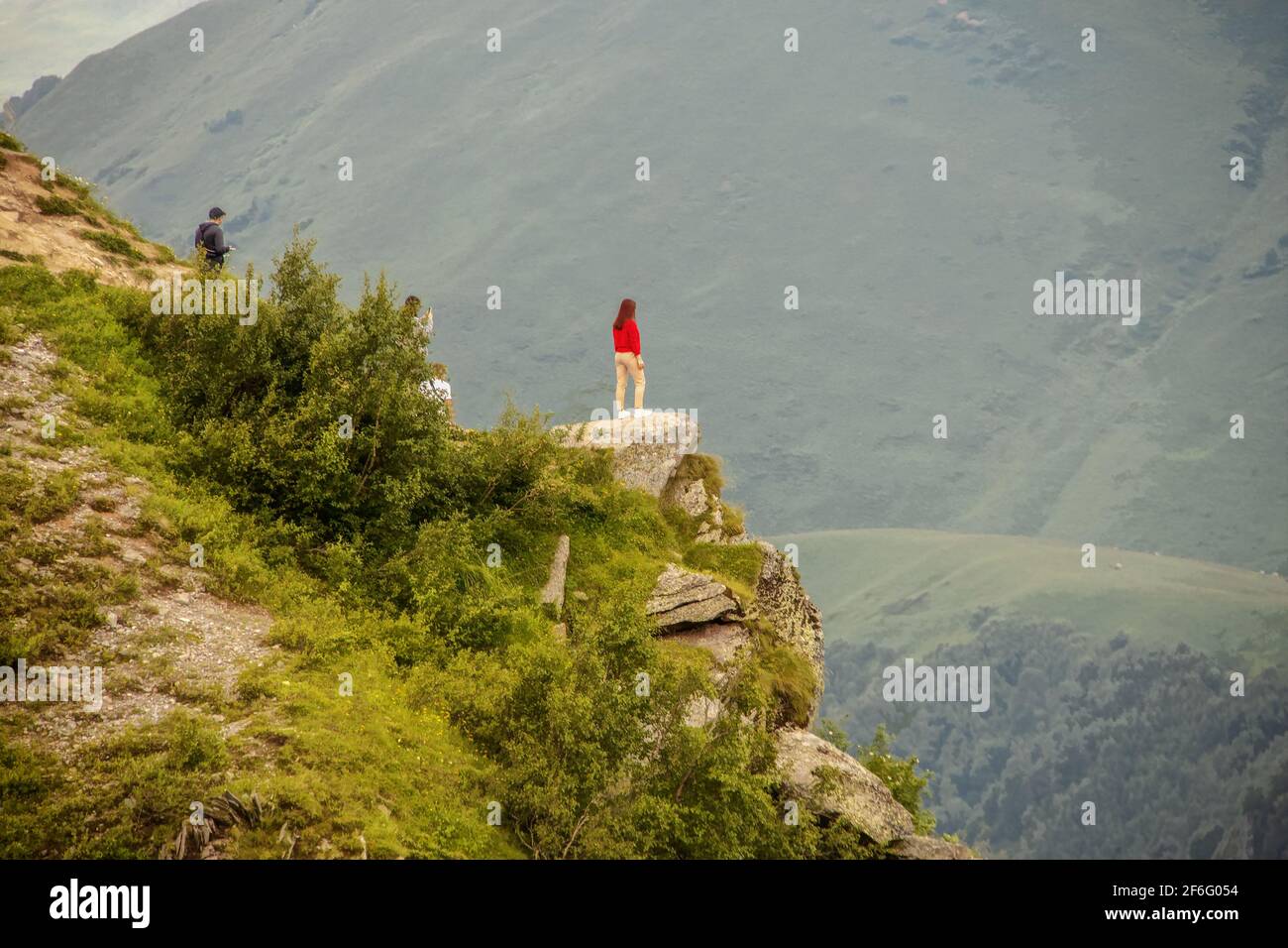 Fille debout sur l'affleurement regardant au-dessus de Devil's Valley dans le Montagnes du Caucase de la République de Géorgie avec des amis derrière prise de photos avec ph Banque D'Images