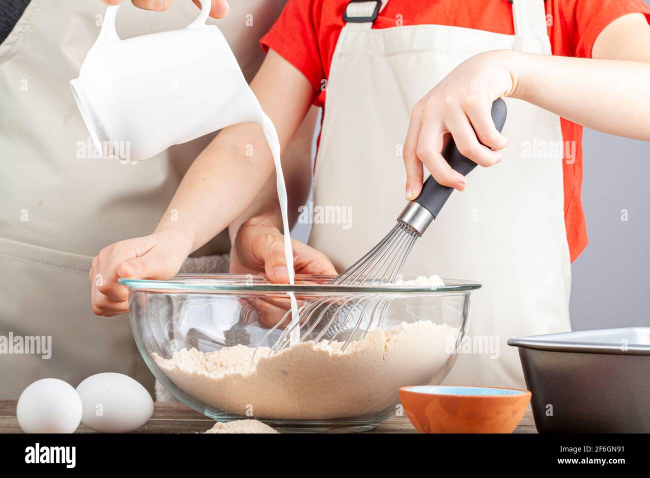 Mère et fille cuisant ensemble dans le concept de cuisine avec la fille tenant un fouet et la femme versant soigneusement lait du pichet dans le m Banque D'Images