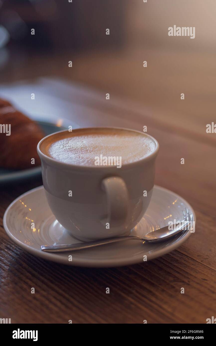 Gros plan sur le cappuccino chaud, latte sur la table avec un arrière-plan flou du café-restaurant. Café au cappuccino chaud sur une table en bois avec un fond croissant flou Banque D'Images