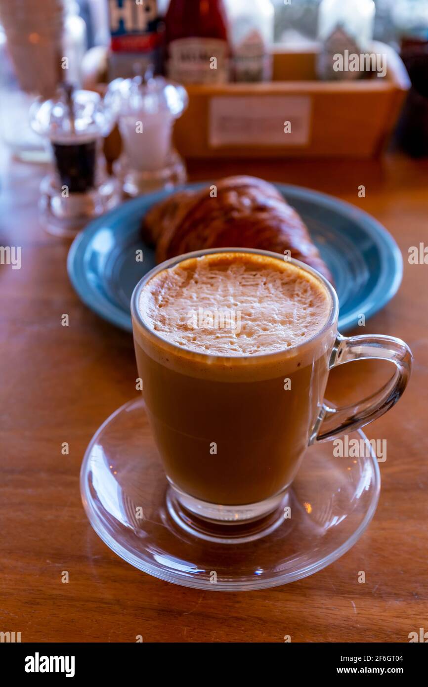 Gros plan sur le cappuccino chaud, le latte, le macchiato caramel sur la table avec un arrière-plan flou du café. Café cappuccino chaud sur table en bois avec croissant flou b Banque D'Images