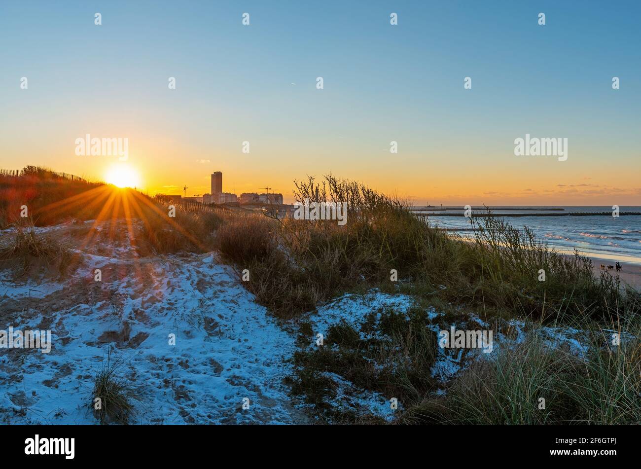 Oostende (Ostende) dunes de sable coucher de soleil avec neige au bord de la mer du Nord avec étoile du soleil, Flandre, Belgique. Banque D'Images
