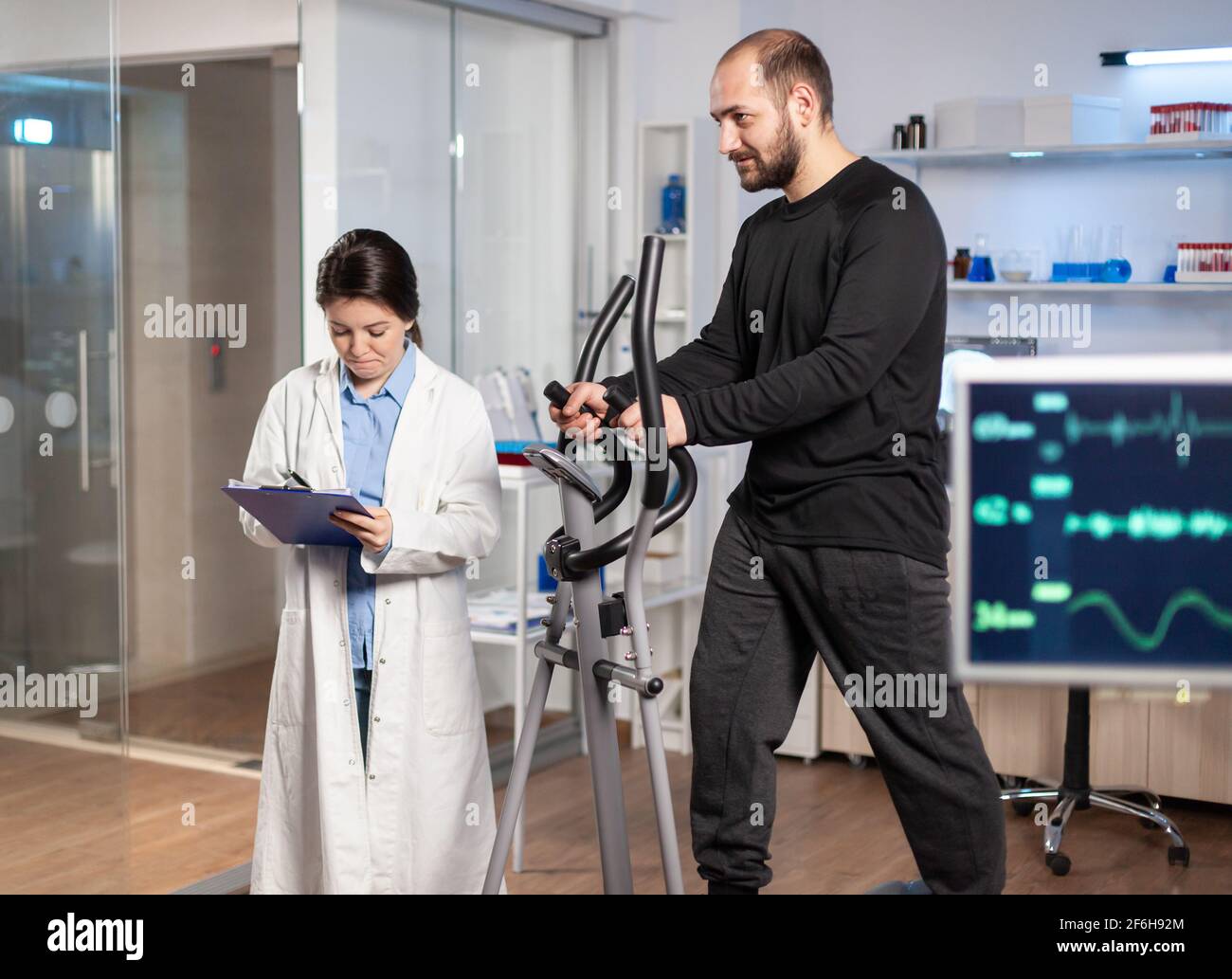Chercheur sportif en laboratoire prenant des notes pendant que l'athlète musculaire est en train de courir, examen de la fréquence cardiaque. Test d'endurance dans un laboratoire de biomécanique professionnel. Banque D'Images