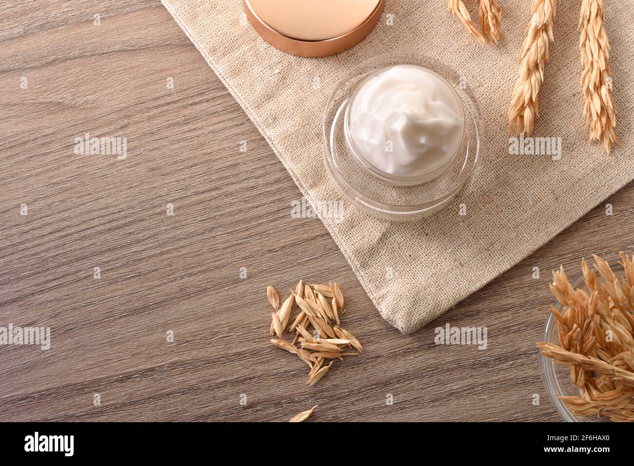 Crème hydratante naturelle avec extrait d'avoine dans un pot en verre toile en toile de jute avec pointes sur table en bois, vue sur le dessus Banque D'Images