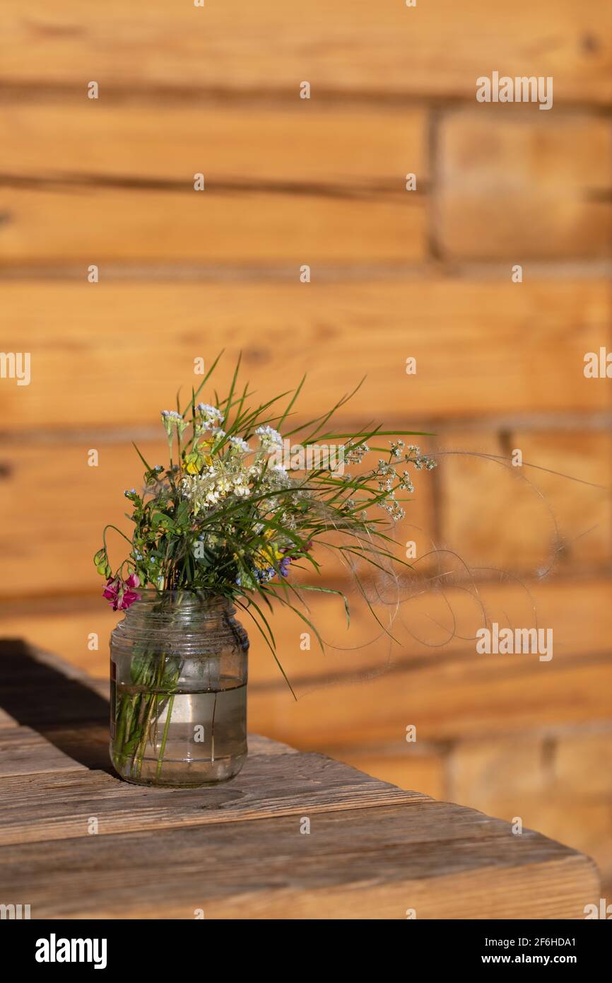 Un modeste bouquet de fleurs sauvages blanches et roses avec des brindilles vertes dans un pot en verre est placé sur une table en bois dans la porte d'entrée. L'été encore la vie. Des souvenirs agréables. Banque D'Images