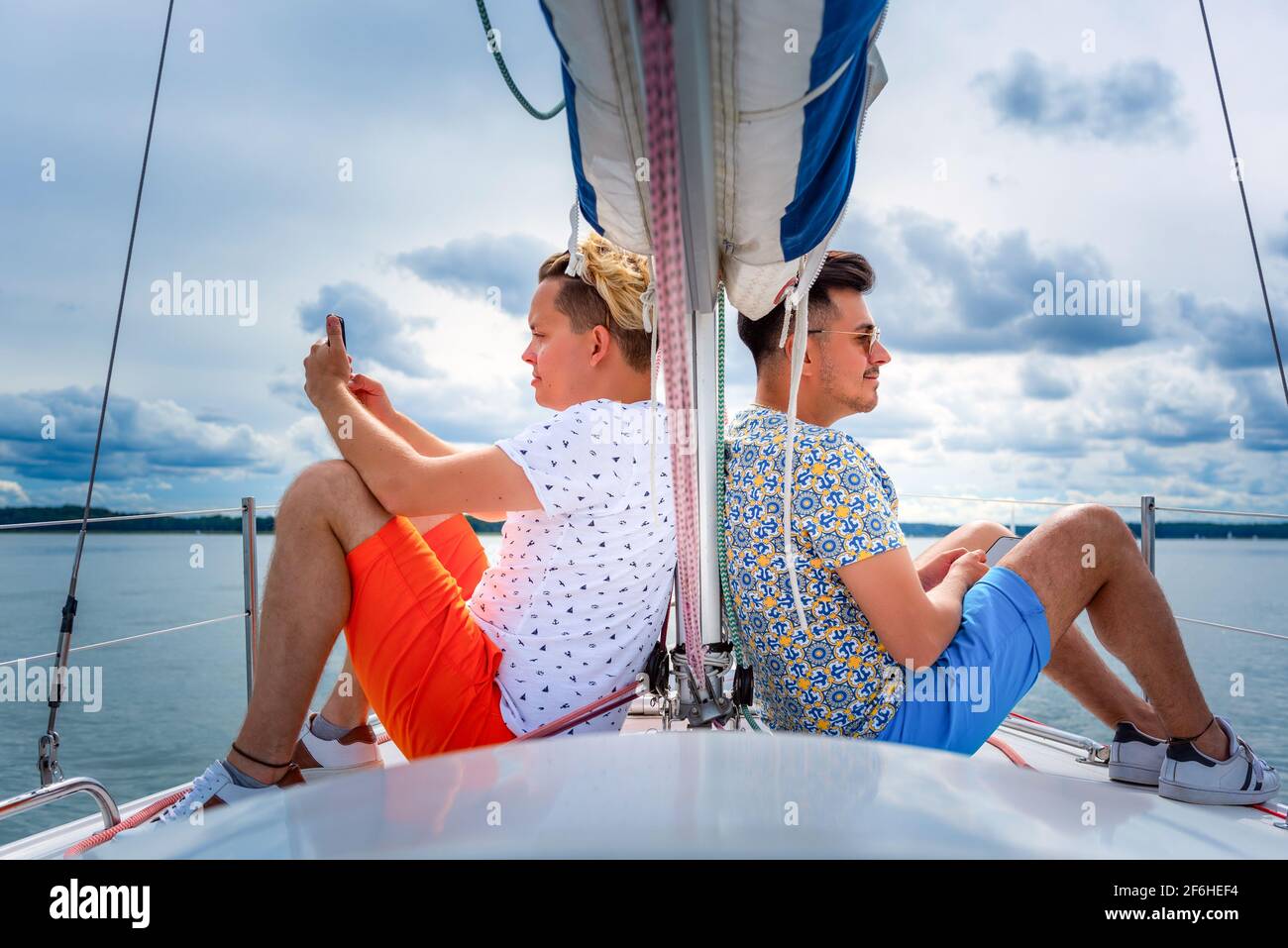 deux jeunes hommes assis sur un pont de voilier bow adn regardant des côtés opposés. vacances de couple gay sur un yacht Banque D'Images