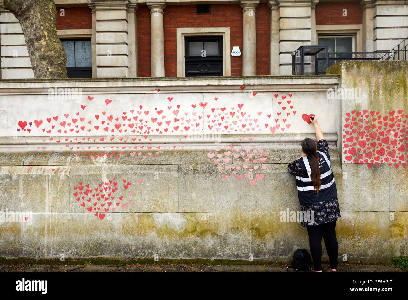 Londres, Royaume-Uni - 31 mars 2021 : la famille et les amis des victimes de Covid-19 peignent des coeurs rouges au mur commémoratif national de Covid, en face de l'hôpital St. Thomas, dans le centre de Londres. Chaque cœur tiré individuellement représente une victime du coronavirus. Banque D'Images