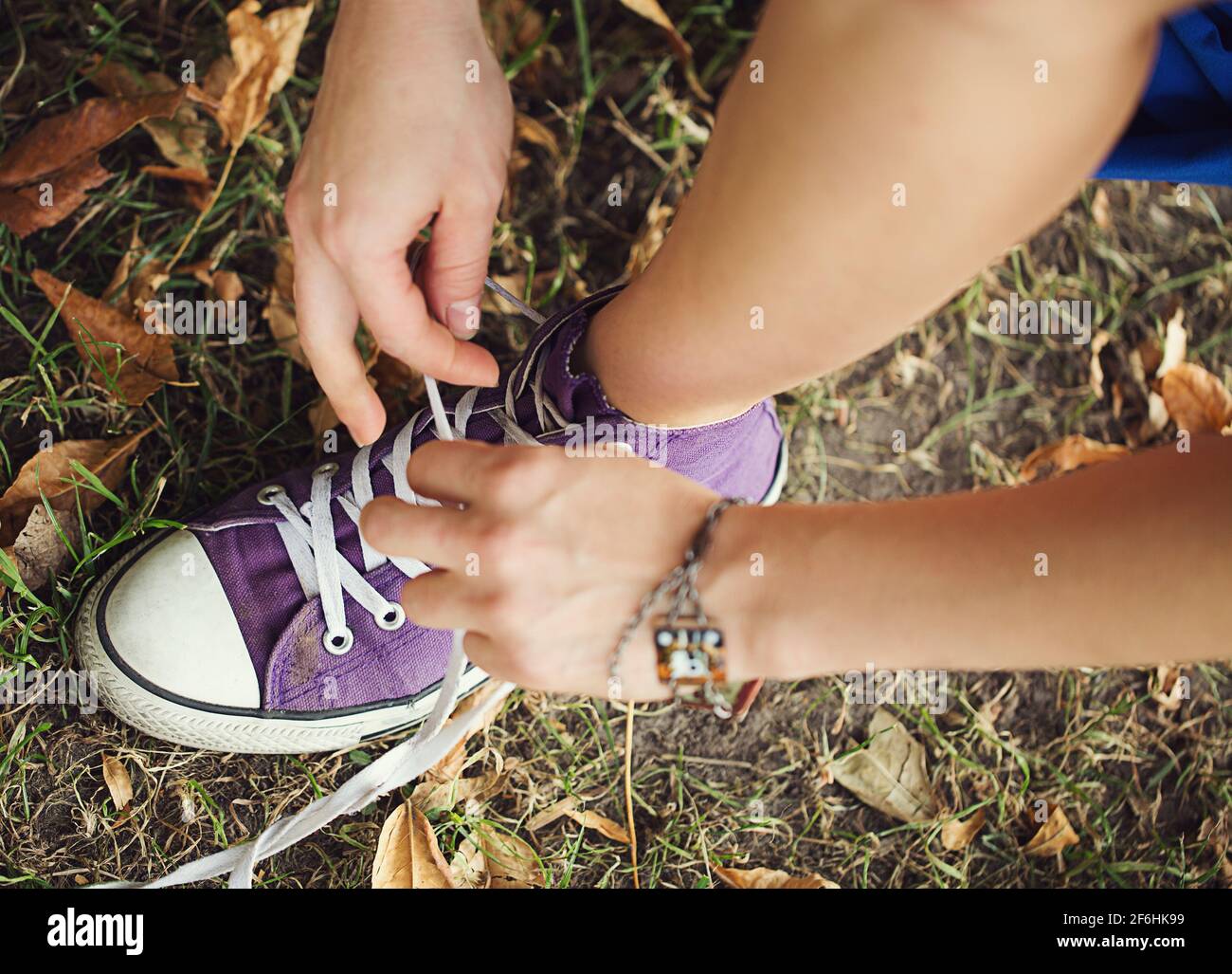 Une fille attache des lacets blancs sur des sneakers lilas, gros plan, sur  un fond d'herbe et de feuilles, vue du dessus Photo Stock - Alamy