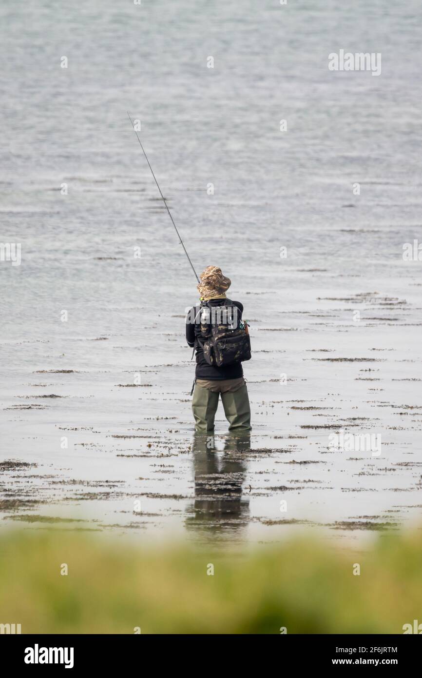 Un pêcheur portant des waders tenant une canne à pêche Banque D'Images