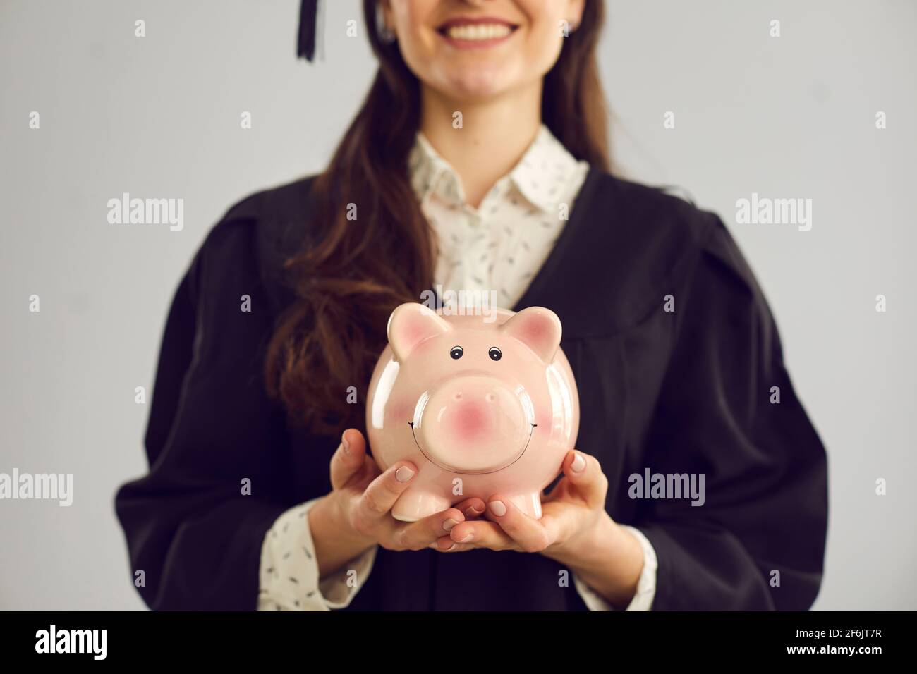 Image rognée gros plan d'une banque de porc dans les mains d'une étudiante sur fond gris. Banque D'Images
