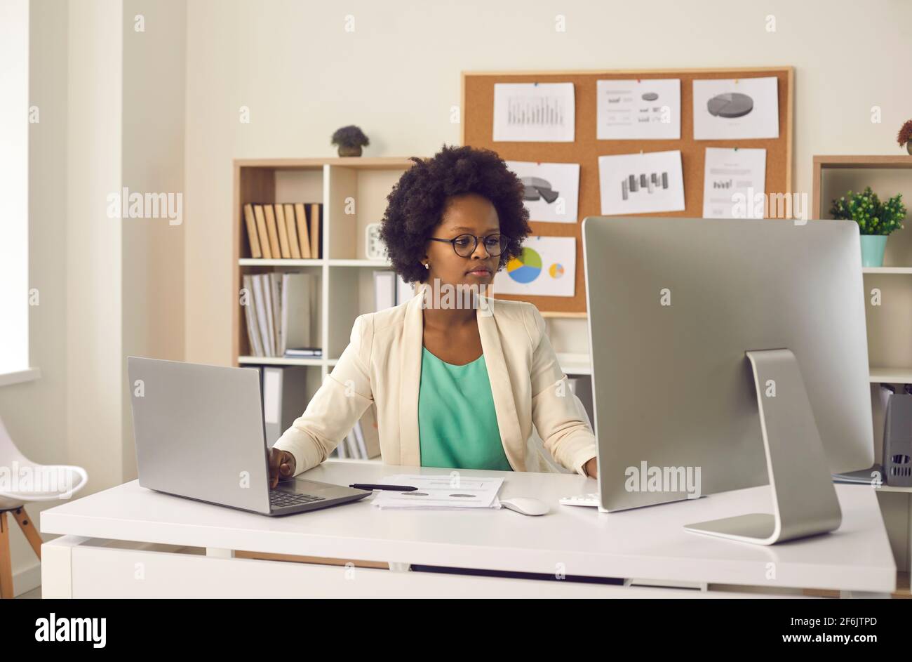 Femme secrétaire travaille avec des documents d'affaires électroniques simultanément sur un ordinateur et un ordinateur portable. Banque D'Images