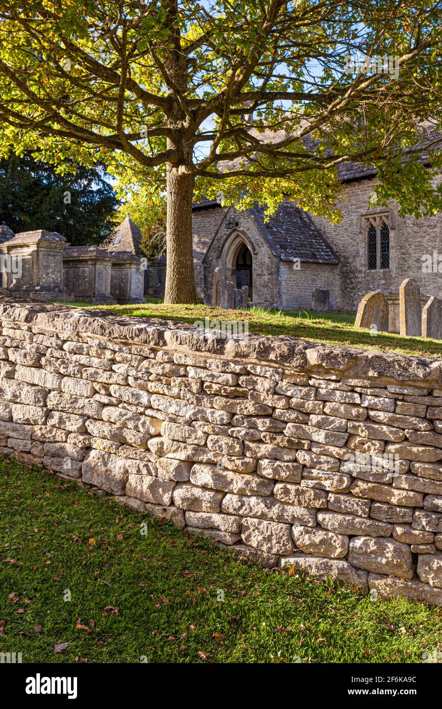 Lumière du soir sur le mur de pierre sec entourant la petite église normande de St Michael dans le village de Cotswold de Winson, Gloucestershire, Royaume-Uni. Banque D'Images