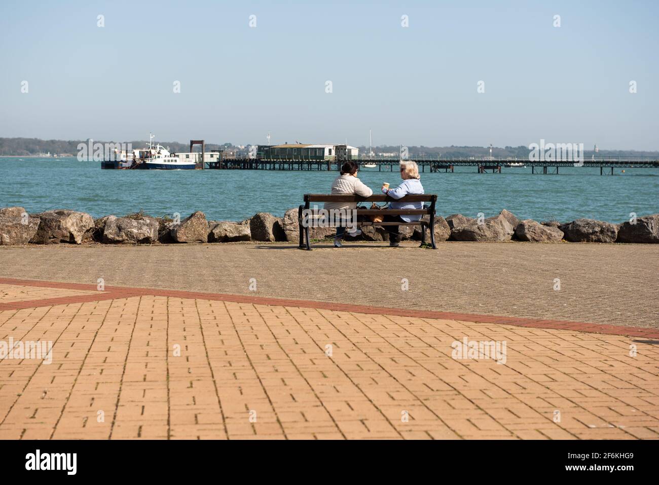 Les personnes âgées ont pris leur retraite pour obtenir de l'air frais assis sur le banc Hythe Vue sur les eaux de Southampton Banque D'Images