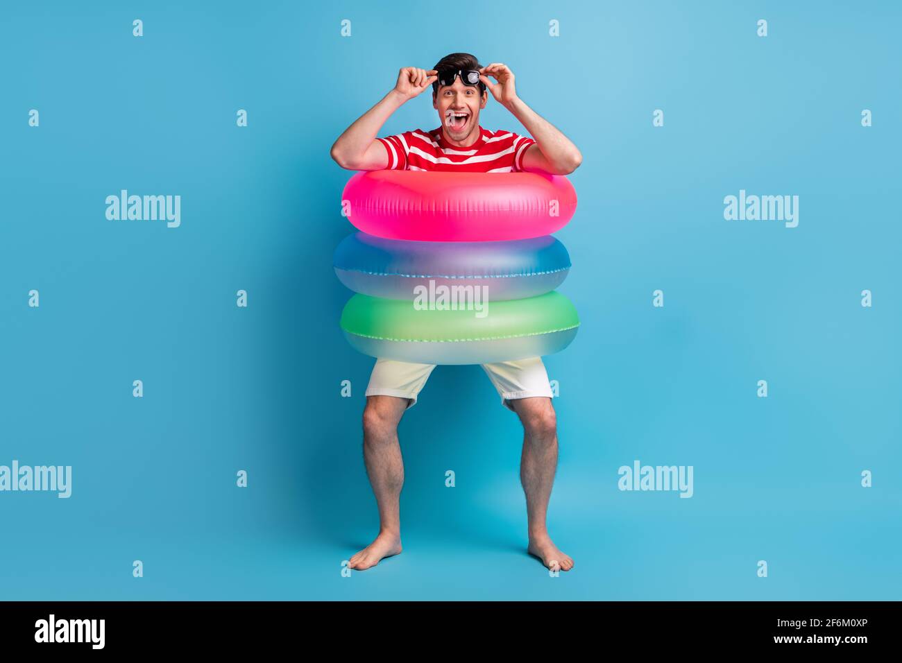 Pleine longueur de corps photo ludique puéril homme va porter coloré cercles en caoutchouc riant isolés sur fond bleu vif Banque D'Images